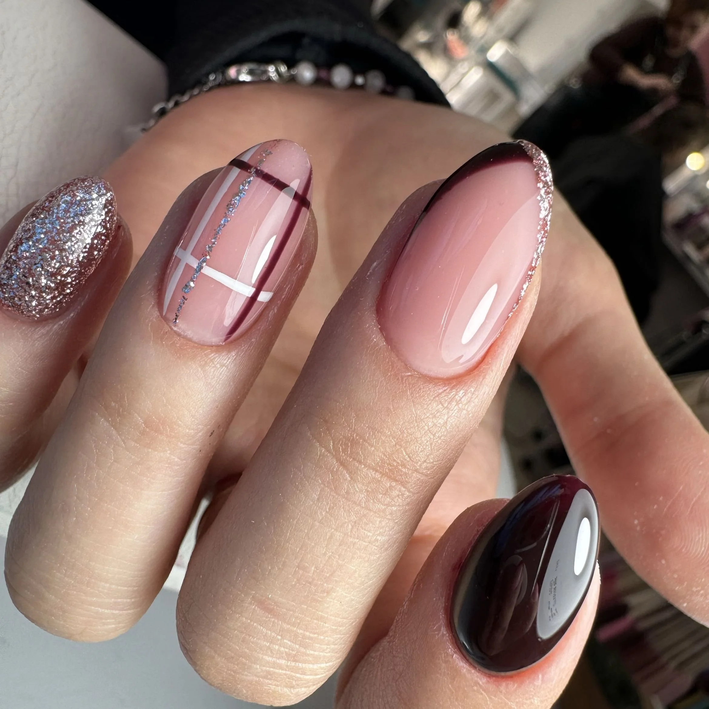 Close-up of a hand with decorated nails featuring various designs, including glitter, plaid, and gradient effects.