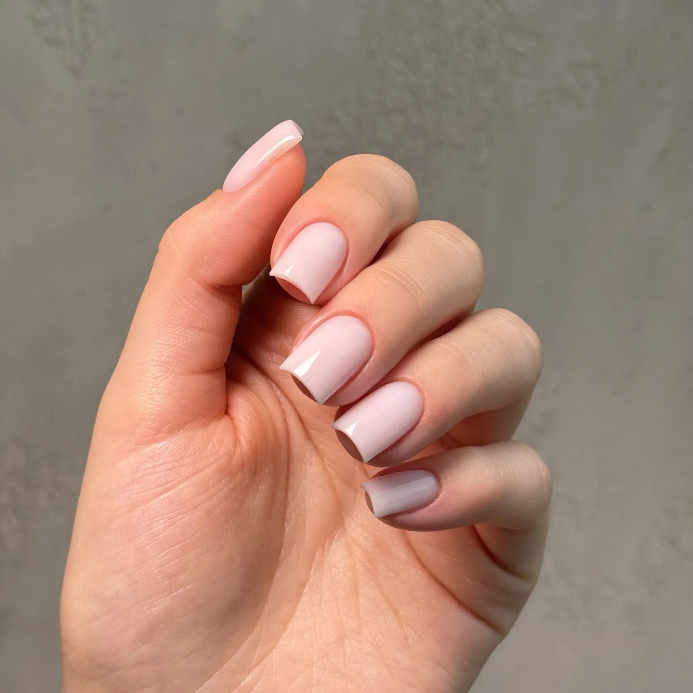 Close-up of a hand with neatly manicured nails painted in a glossy pale pink color.