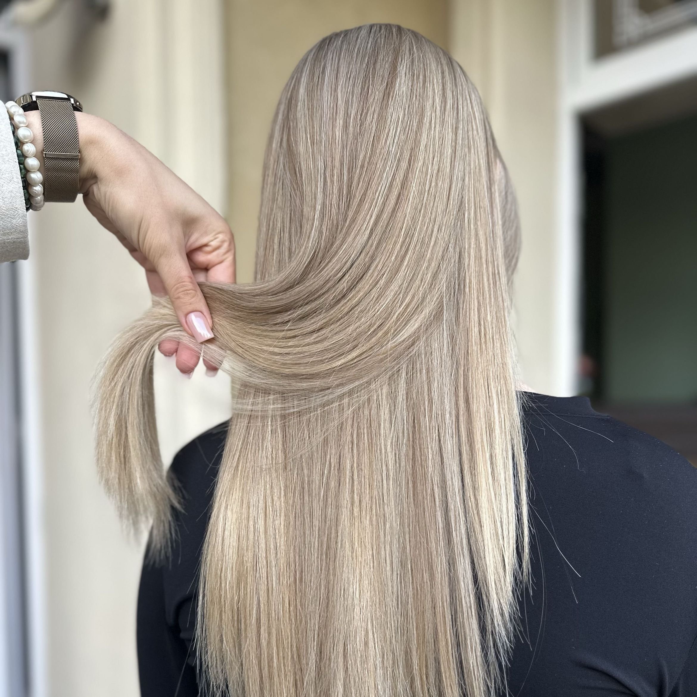 Person with long, straight, blonde hair being held and styled by a hand.