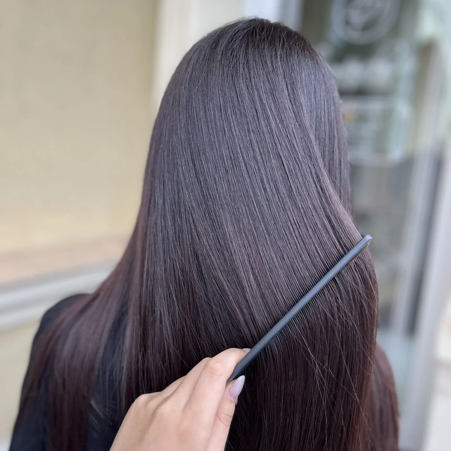 Close-up of a person with long, shiny, straight brown hair being combed with a black comb.