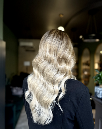 Back of a person with long, wavy platinum blonde hair in an indoor setting.