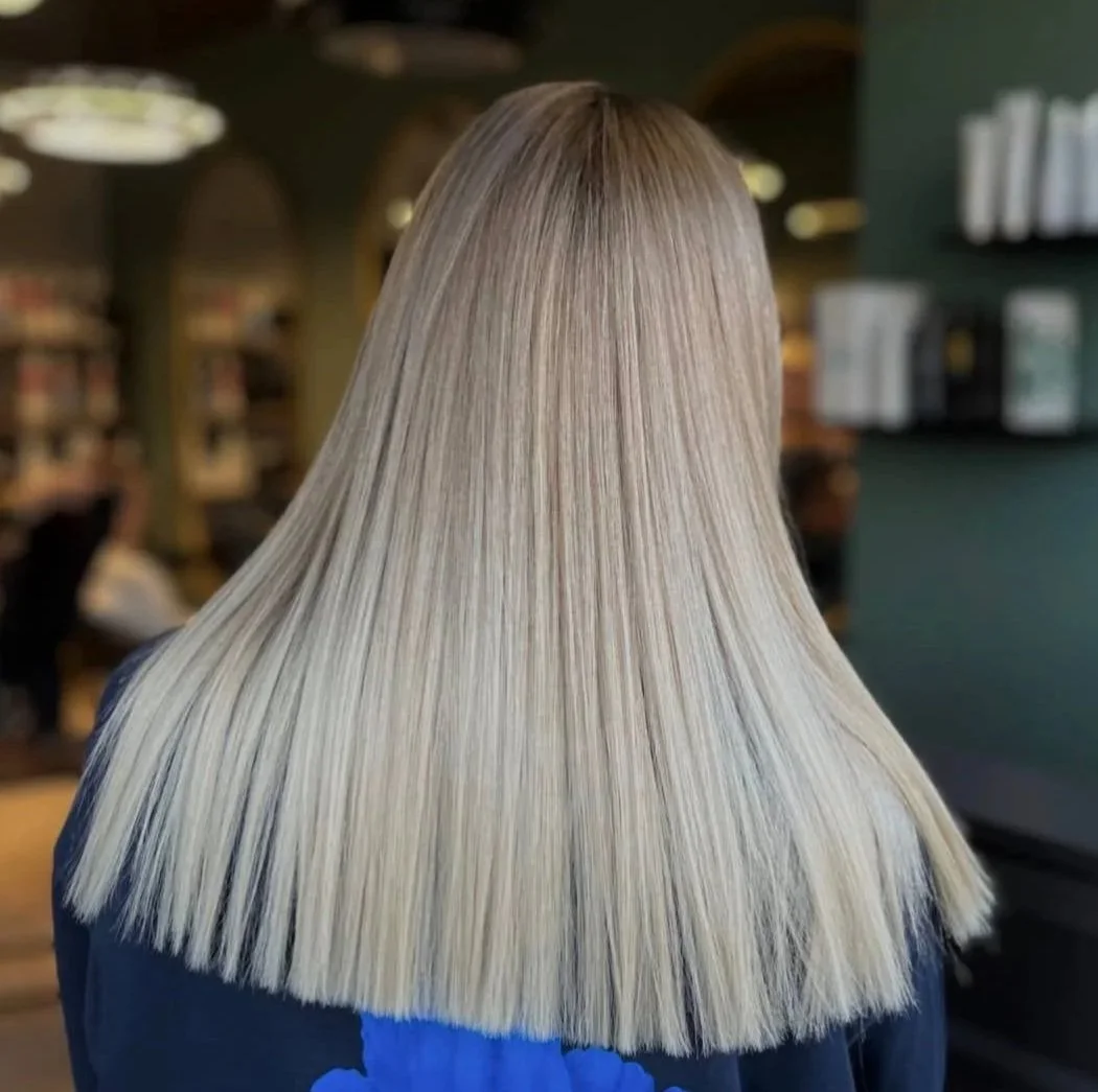 Back of a woman with long, straight, platinum blonde hair in a salon or library setting.
