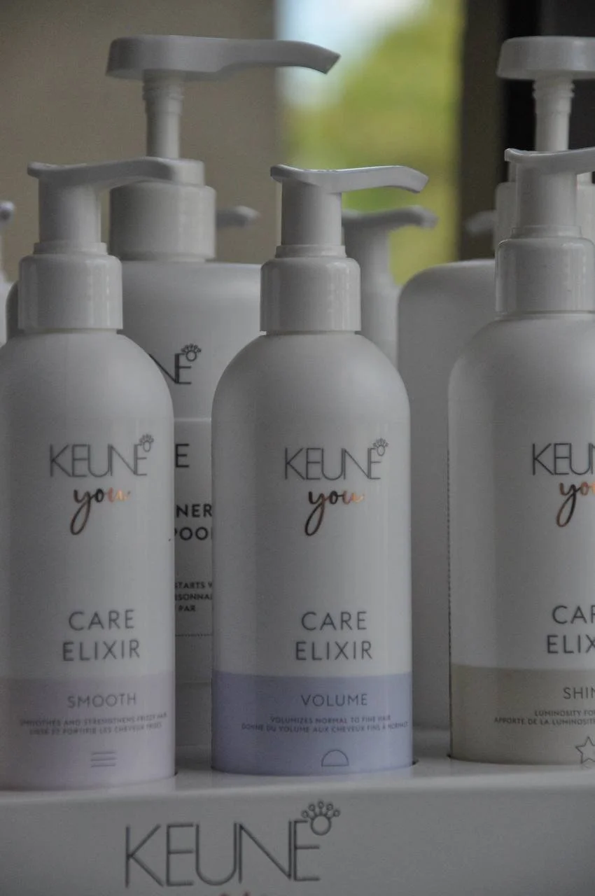 Multiple white bottles of KEUNE hair care products with pump dispensers on a store shelf.