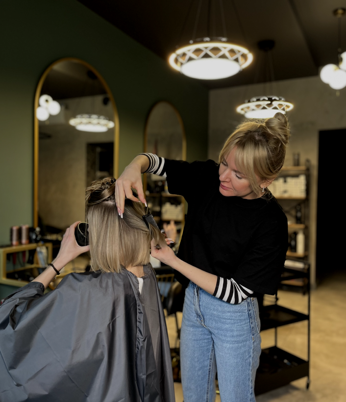 Hairdresser cutting a client's blonde hair in a salon with modern decor and large mirrors.