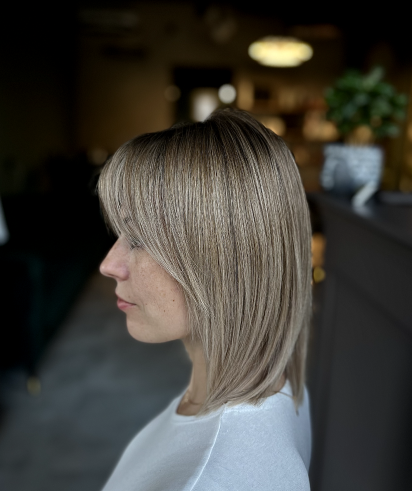 Side profile of a woman with blonde hair in a layered bob hairstyle, indoors with blurred background.
