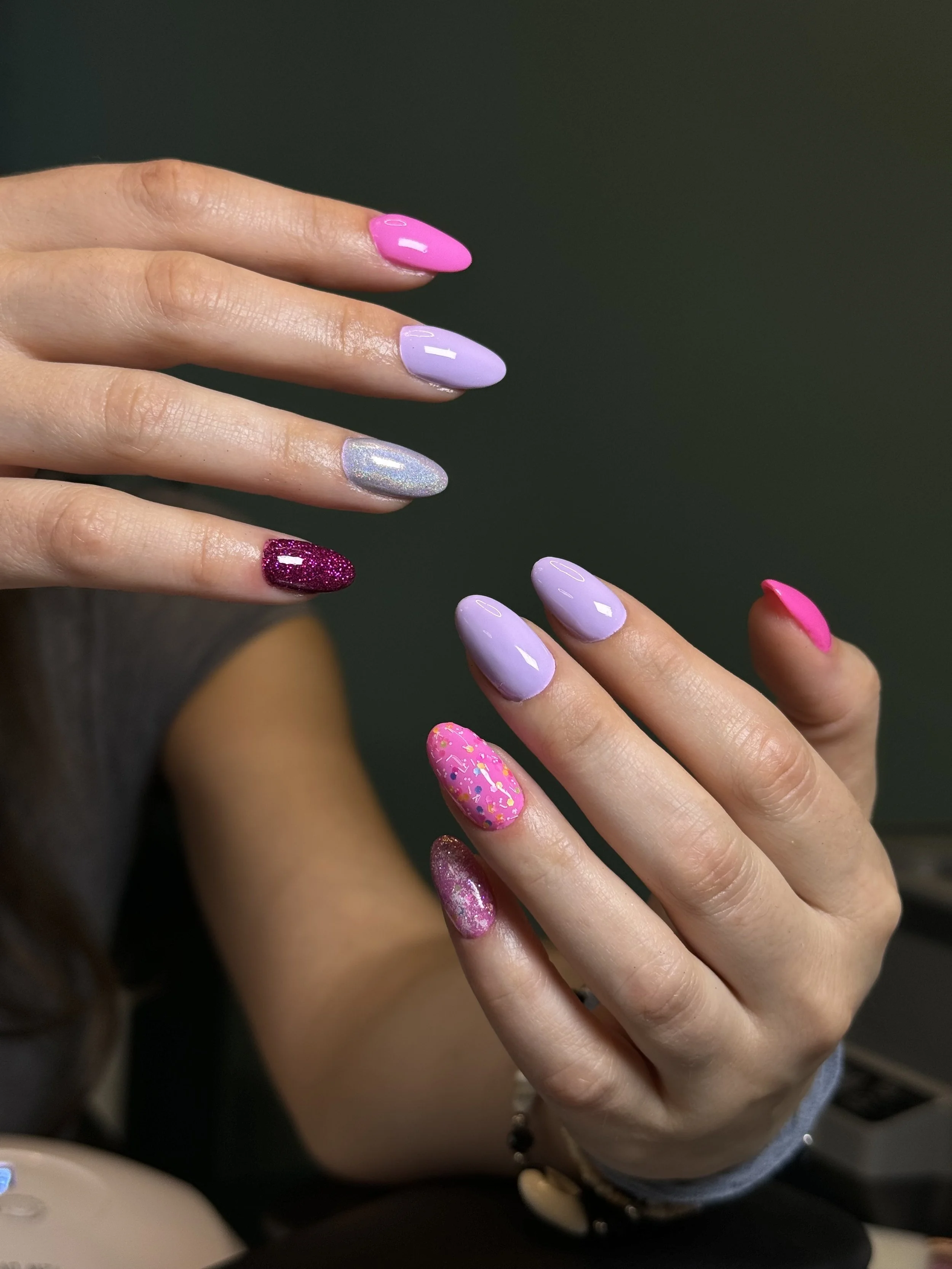 Close-up of hands with colorful manicured nails in pink, purple, glitter, and patterned designs.
