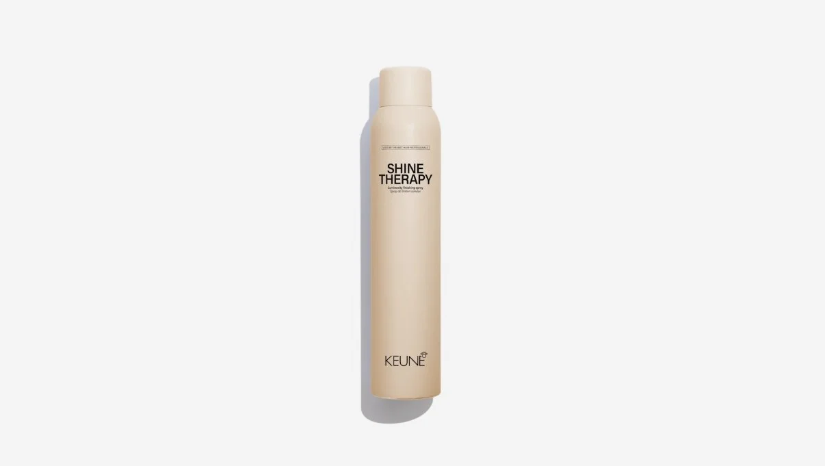 A beige bottle of Keune Shine Therapy Luminosity Finishing Spray with black text on a white background.