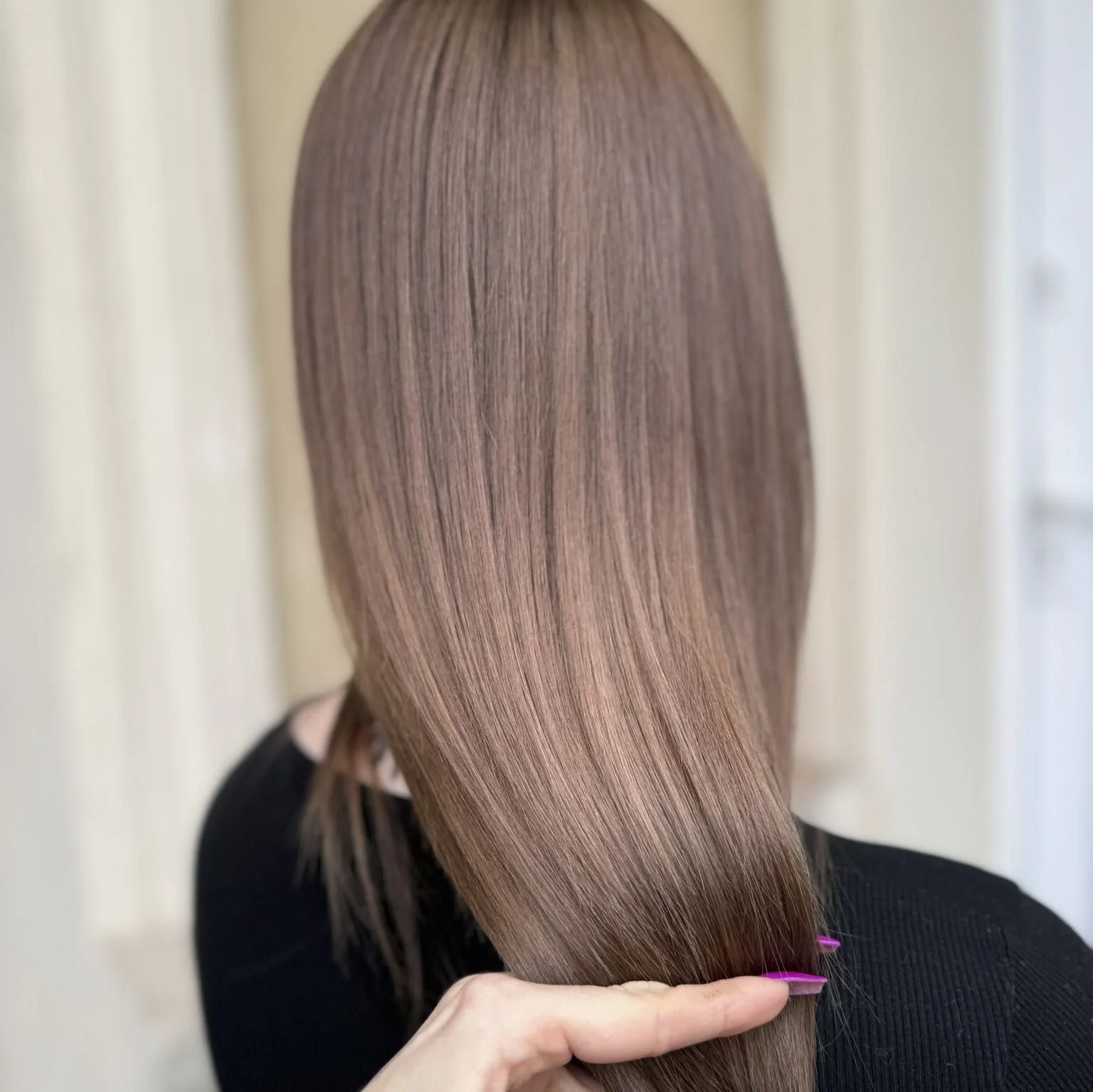 Back view of a person with long, straight, light brown hair being held gently by their hand.