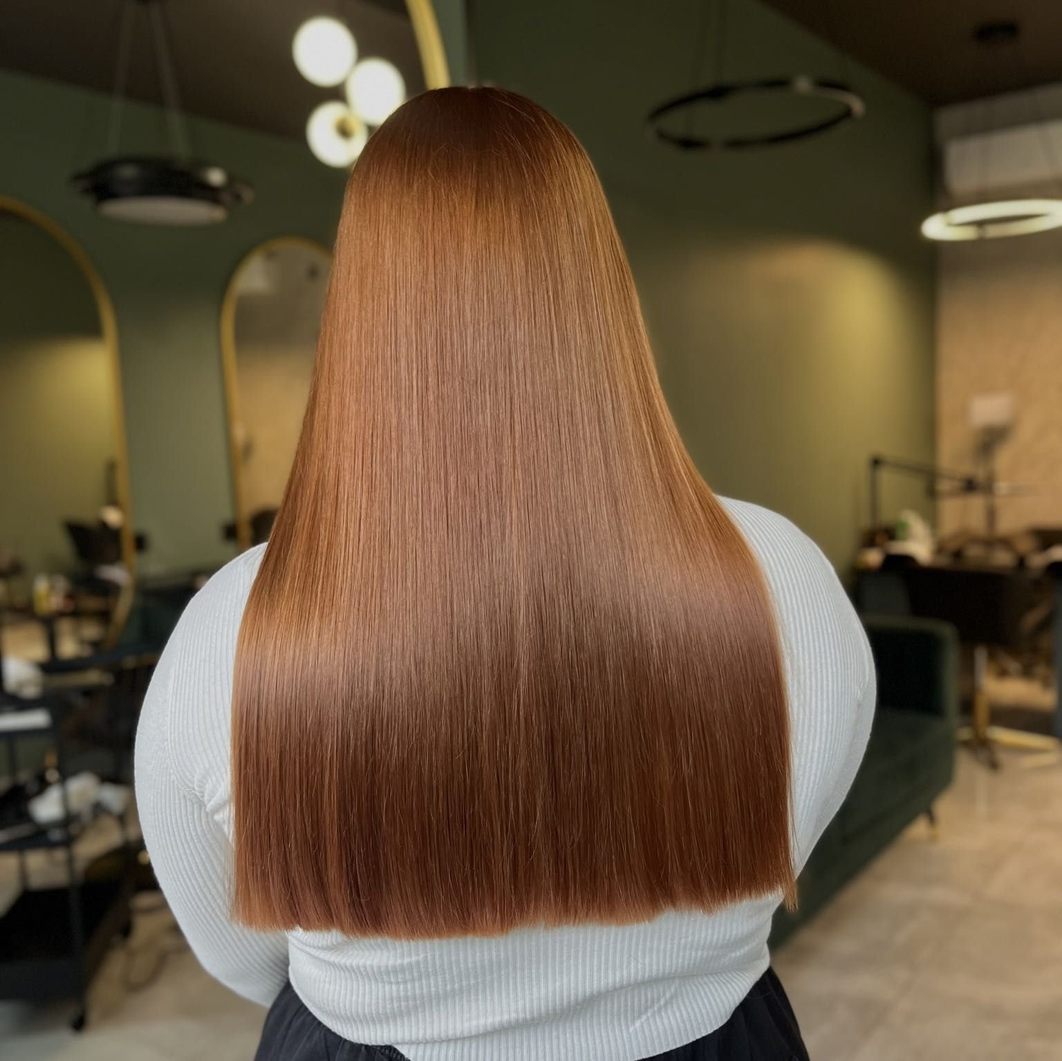 Back of a person with long, straight, reddish-brown hair in a salon.