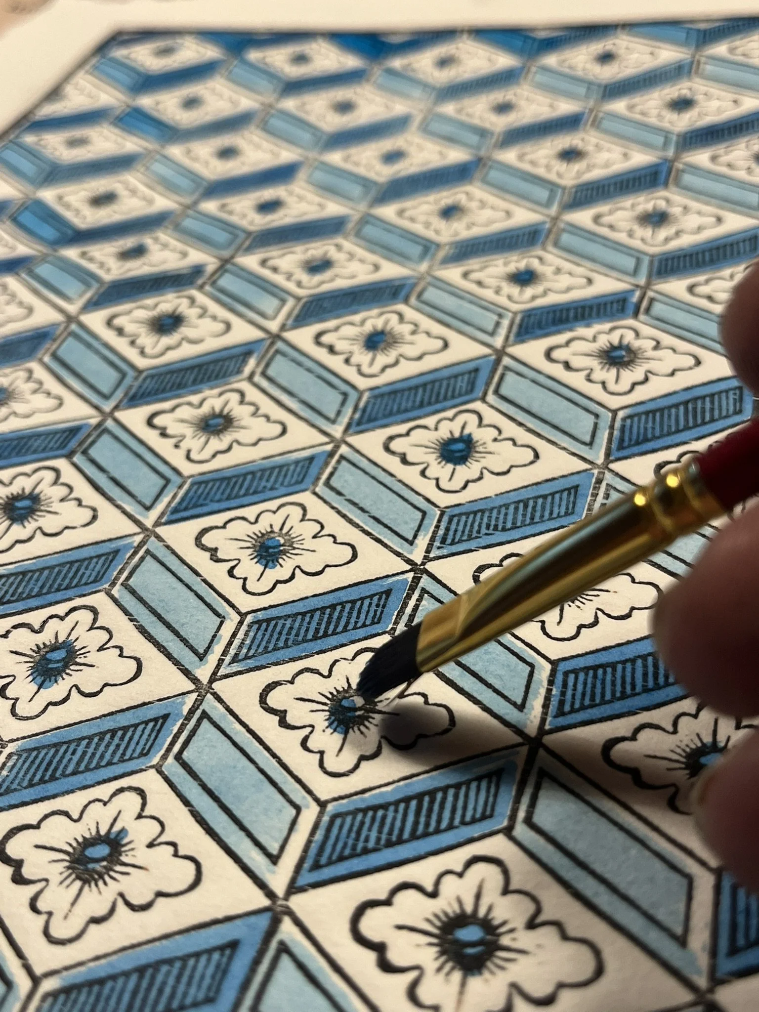 Close-up of a person using a black marker to color in a floral pattern on a piece of patterned paper with blue and black floral and geometric designs.