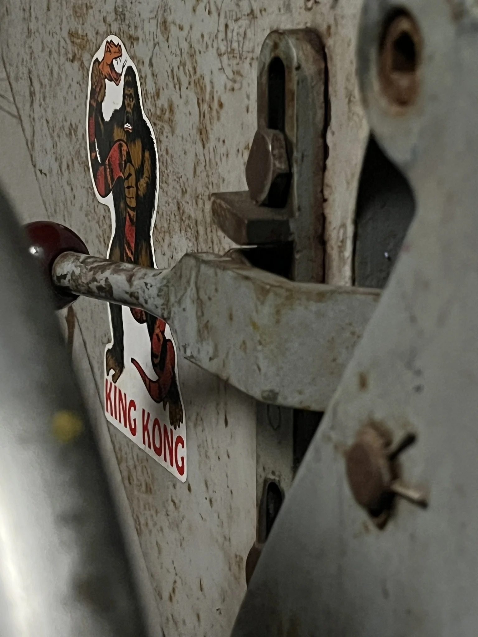 Close-up photo of a worn, dirty metallic surface with an electrical outlet and a sticker of a tiger and a gorilla, with text that reads 'KING KONG'.