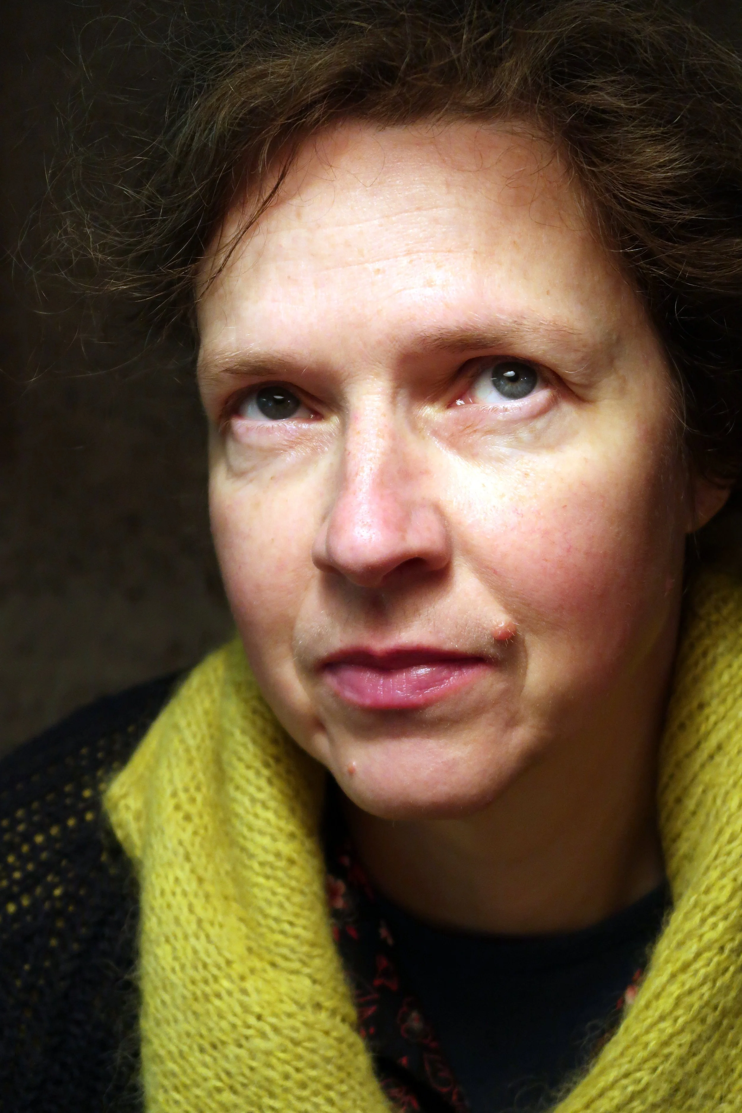 Close-up of a woman's face showing blue eyes, short dark hair, and a yellow knitted scarf.