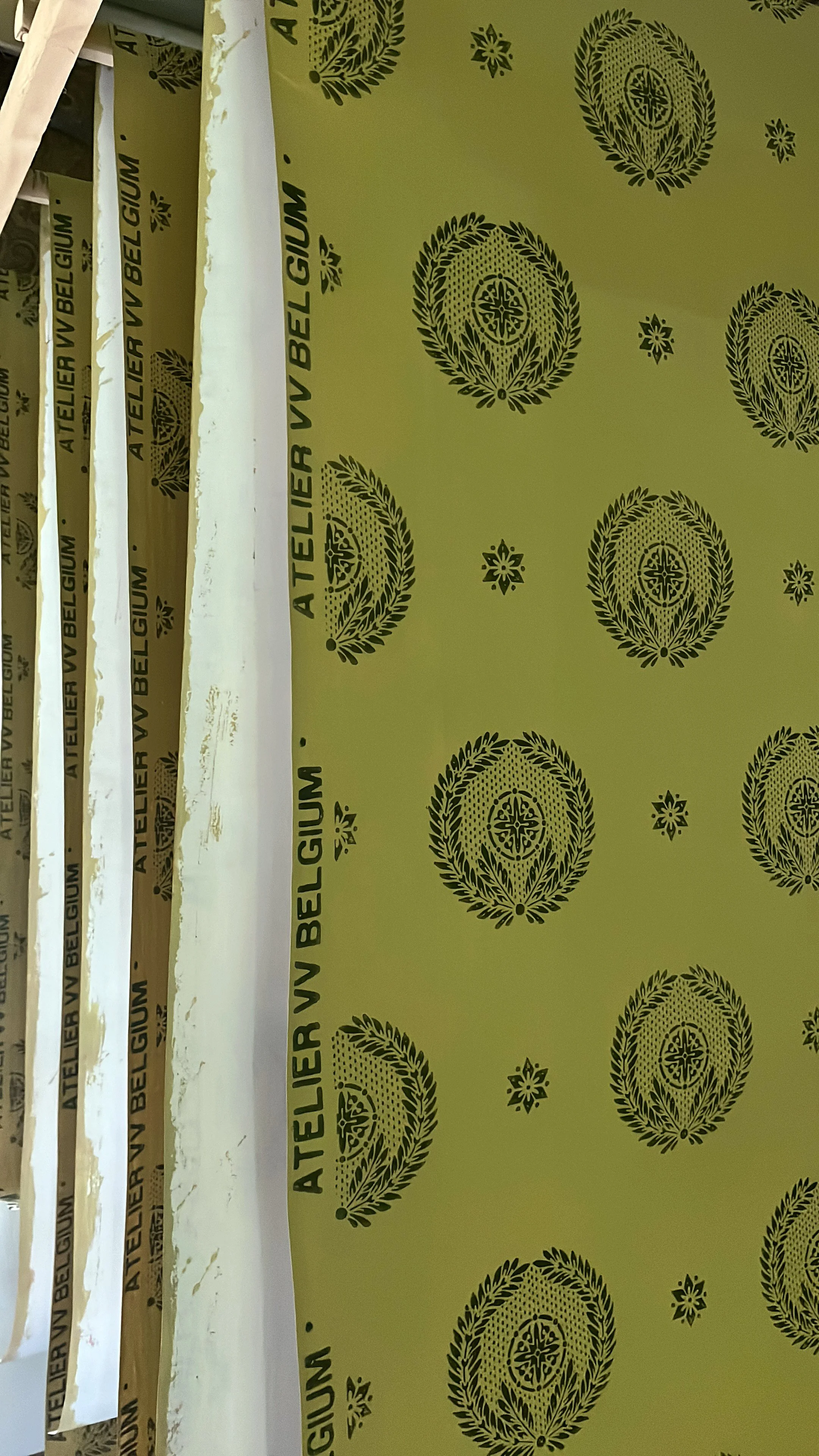 Close-up of yellow drying wallpaper printed with a decorative laurel wreath logo with a cross inside, repeated multiple times.