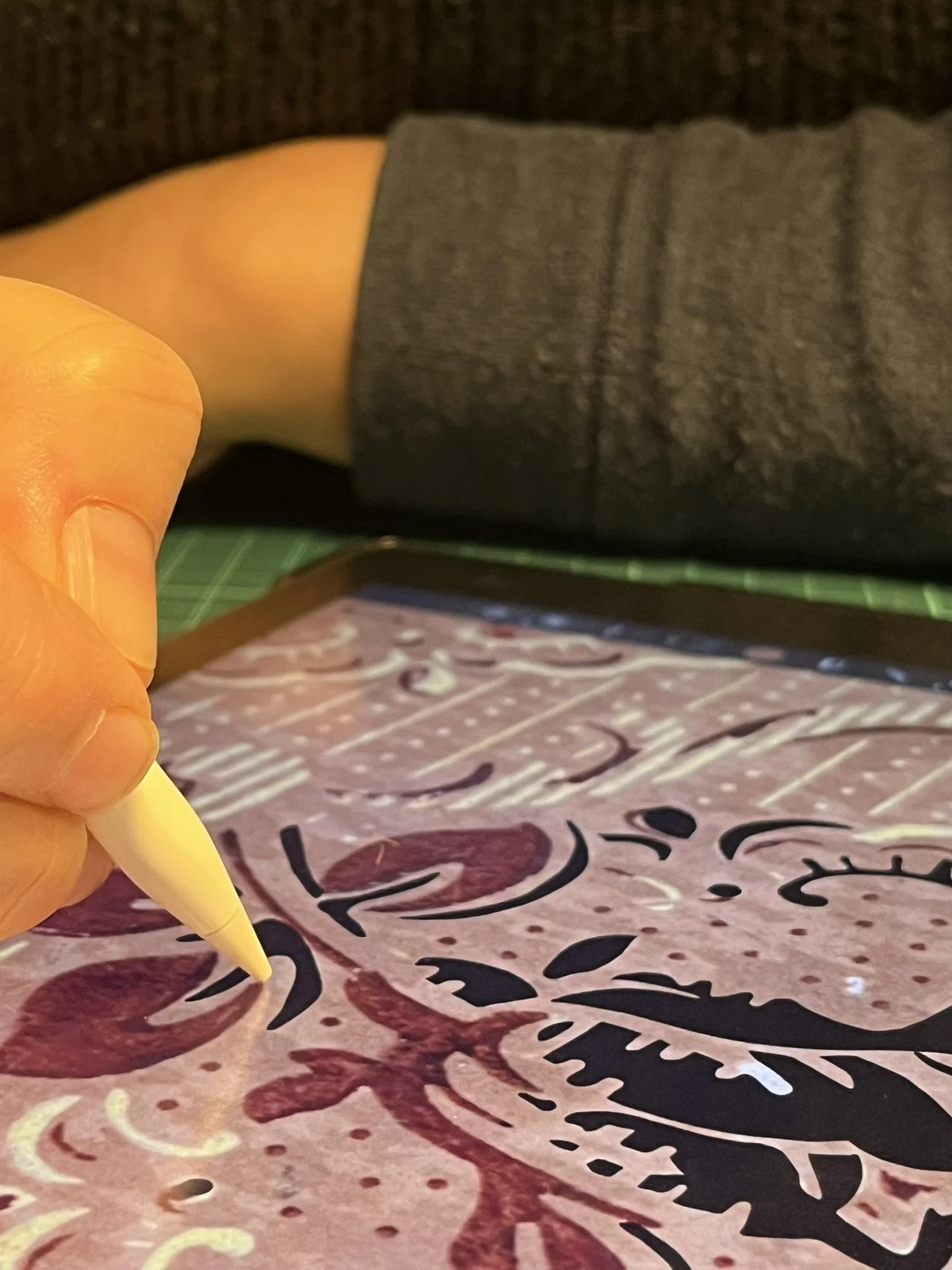 A person holding a yellow pen above a piece of paper with red and black calligraphy or decorative writing.