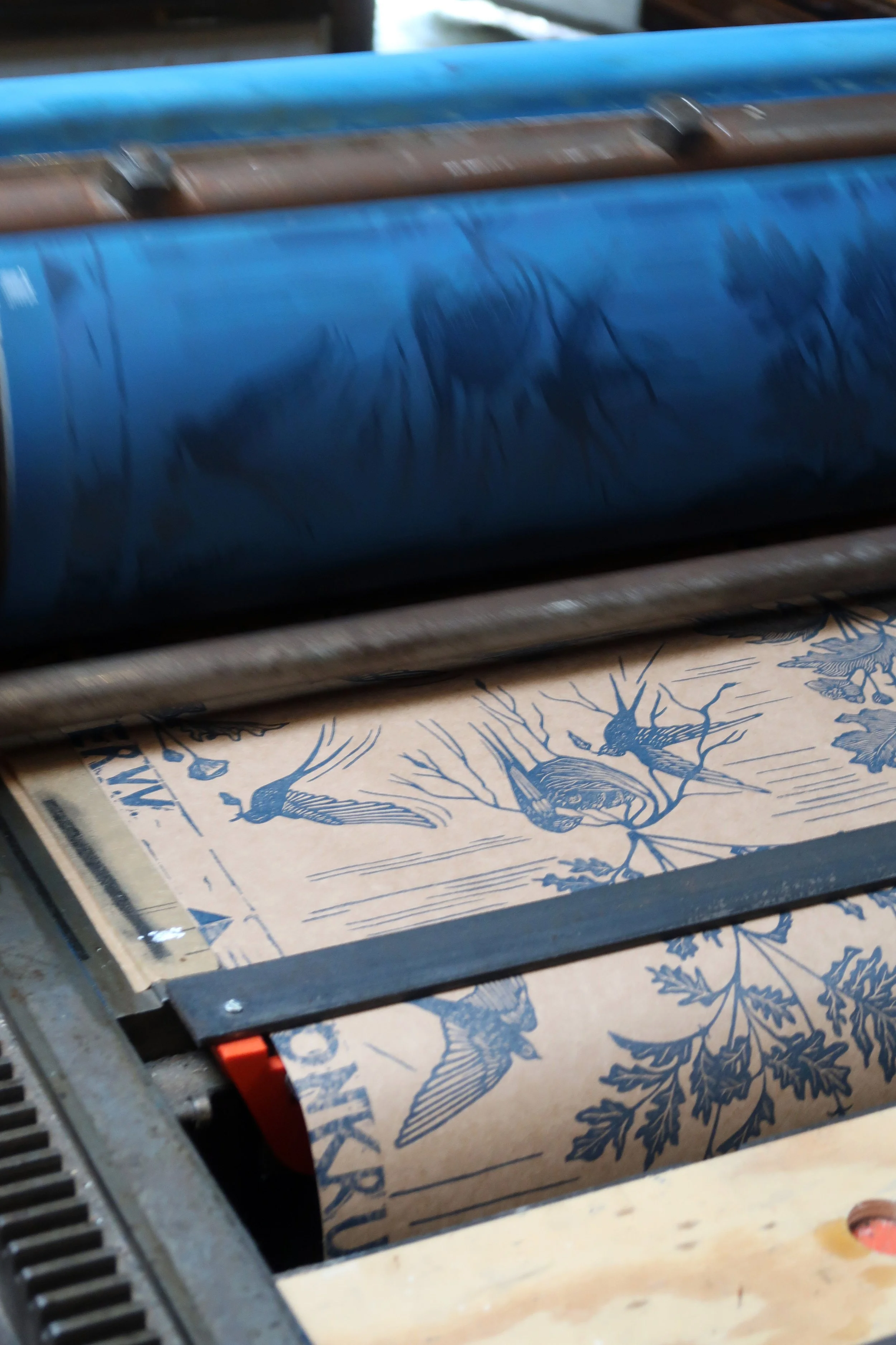 A printing press with paper printed with blue ink featuring birds and tree branches.