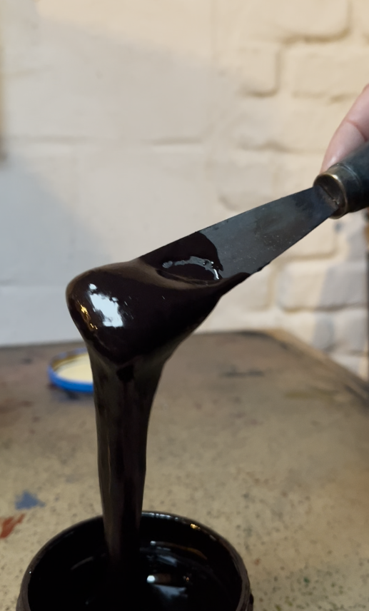 Black paint being stirred with a spatula from a container on a table.