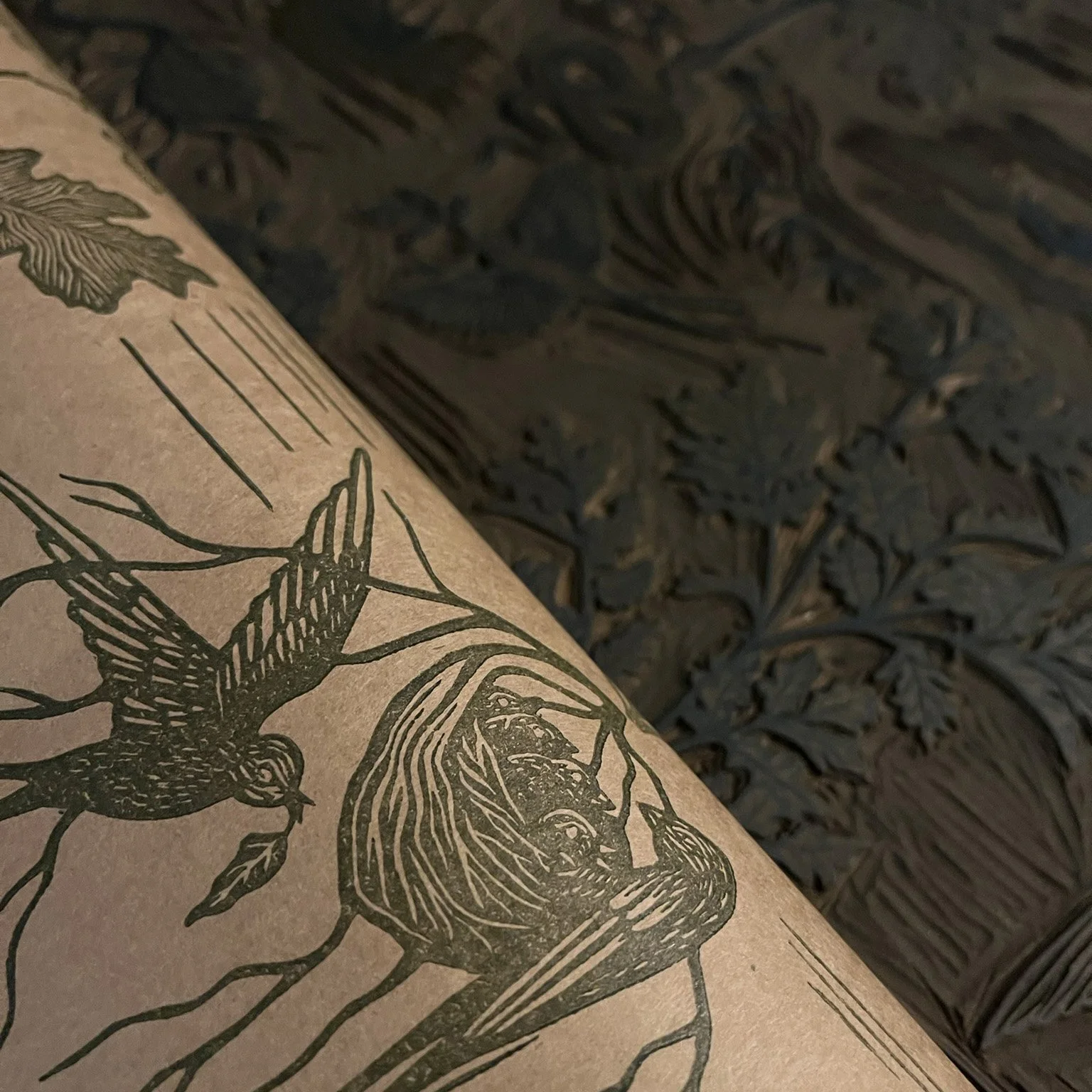 A close-up of a rolled piece of paper or cardboard with an illustration of a bird and plants, and black ink lines, resting on a dark, carved wooden surface with intricate floral and leaf patterns.