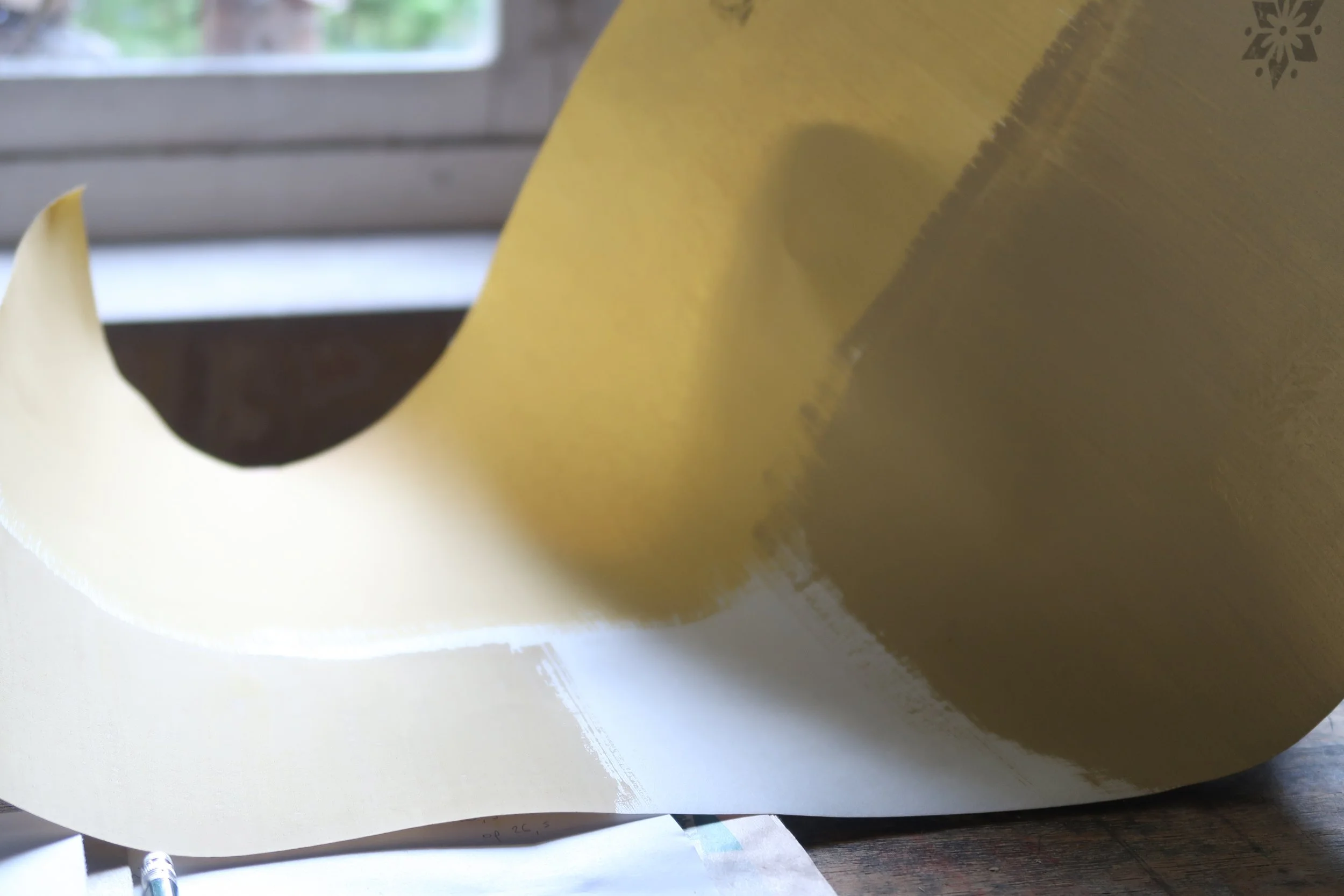 Close-up of a large yellow object being painted or coated with a spray or brush, with a window in the background.