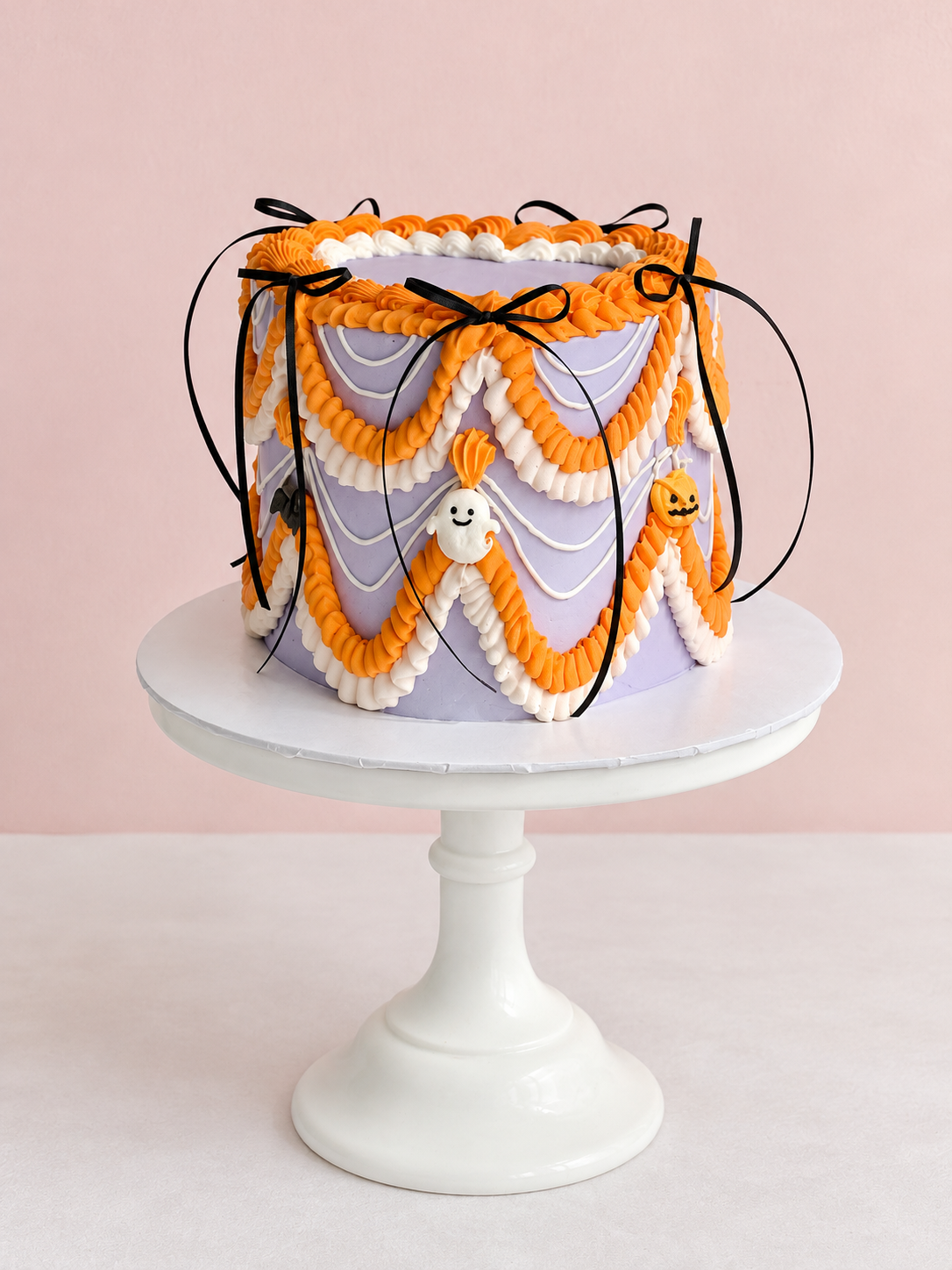 Lavender Midnight Social Halloween cake by Sweet Stacy's Palm Beach with orange and white vintage buttercream piping, black bows, ghosts and pumpkins.