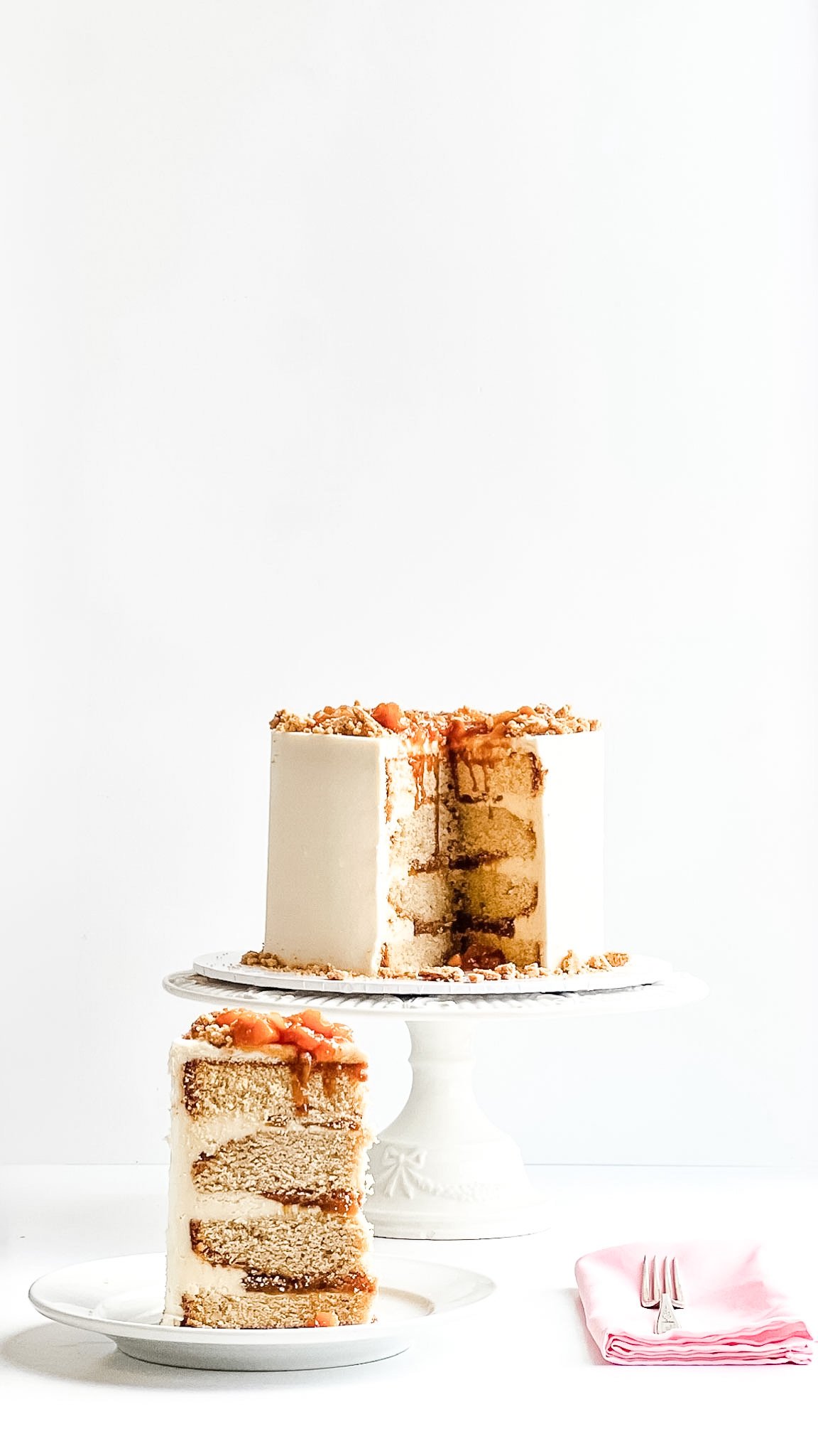 peach cobbler cake set upon a white cake stand with a slice cut out. the slice sitting on a white plate at the forefront of the image showing the cake and cobbler layers