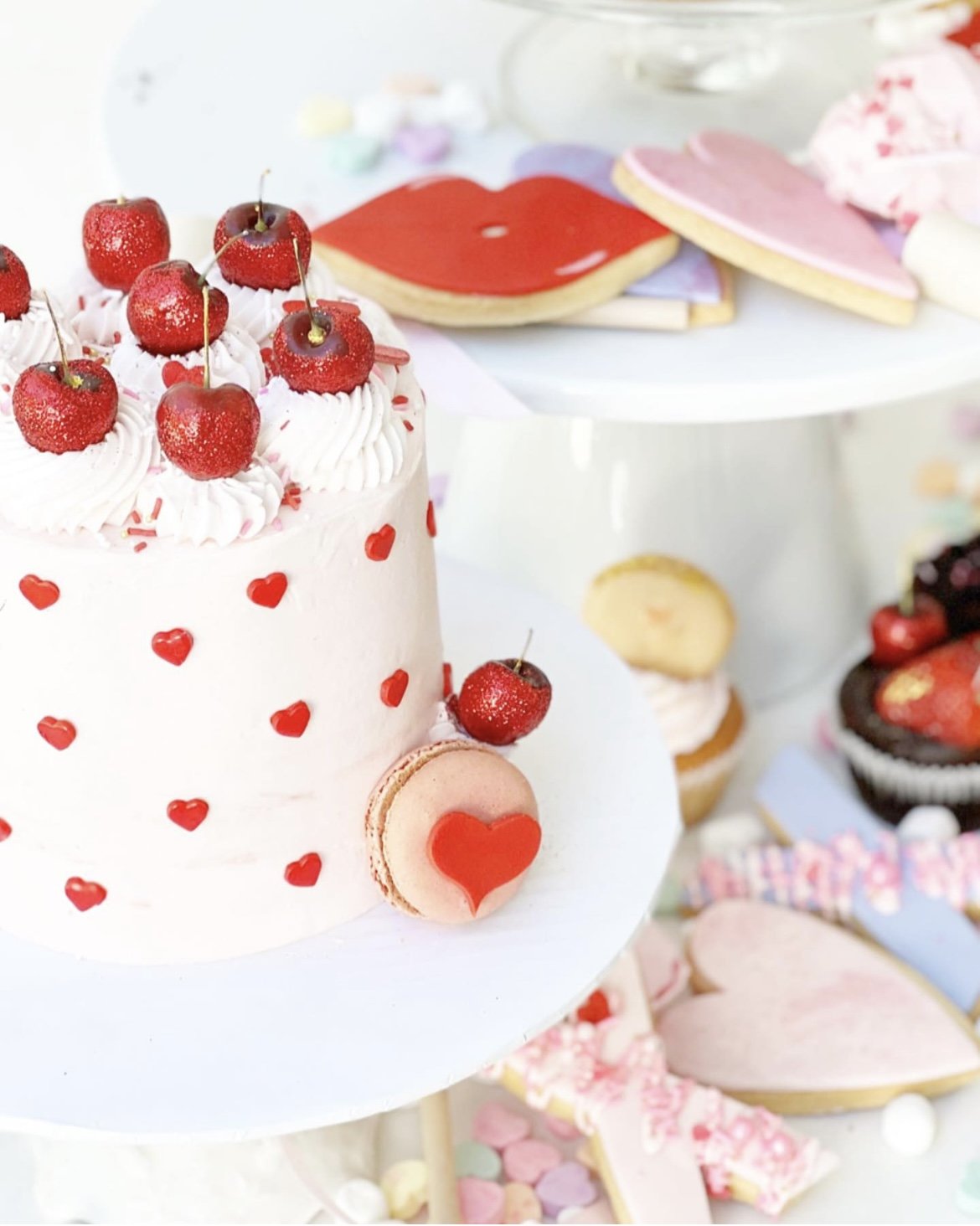 valentines day cake with red hearts and topped with cherries along with lips and heart shaped iced sugar cookies