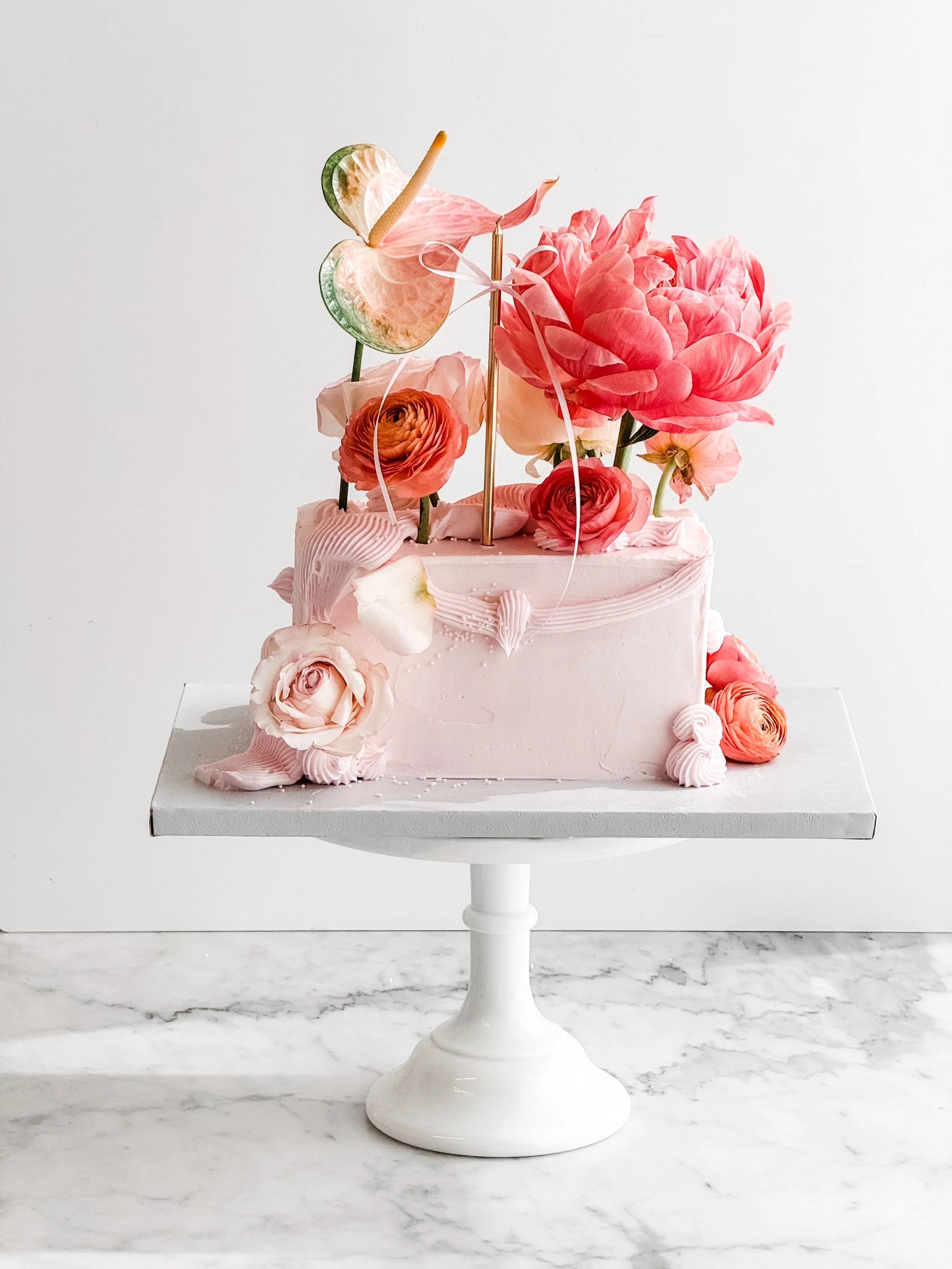 8" bar cake in light pink with florals sitting on a white cake stand