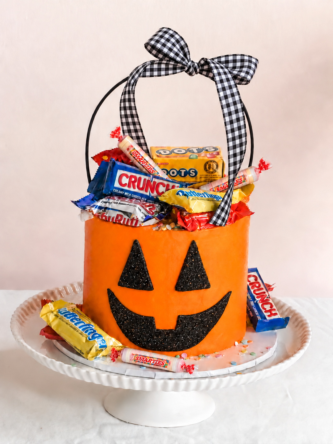Jackie O's Candy Trove Halloween cake by Sweet Stacy's Palm Beach, featuring an orange jack-o'-lantern cake filled with candy and a black-and-white gingham bow.