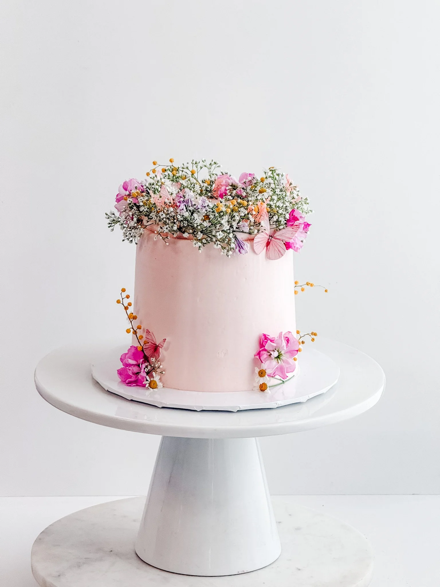 cake on a stand with pink frosting and pink florals and baby breath florals