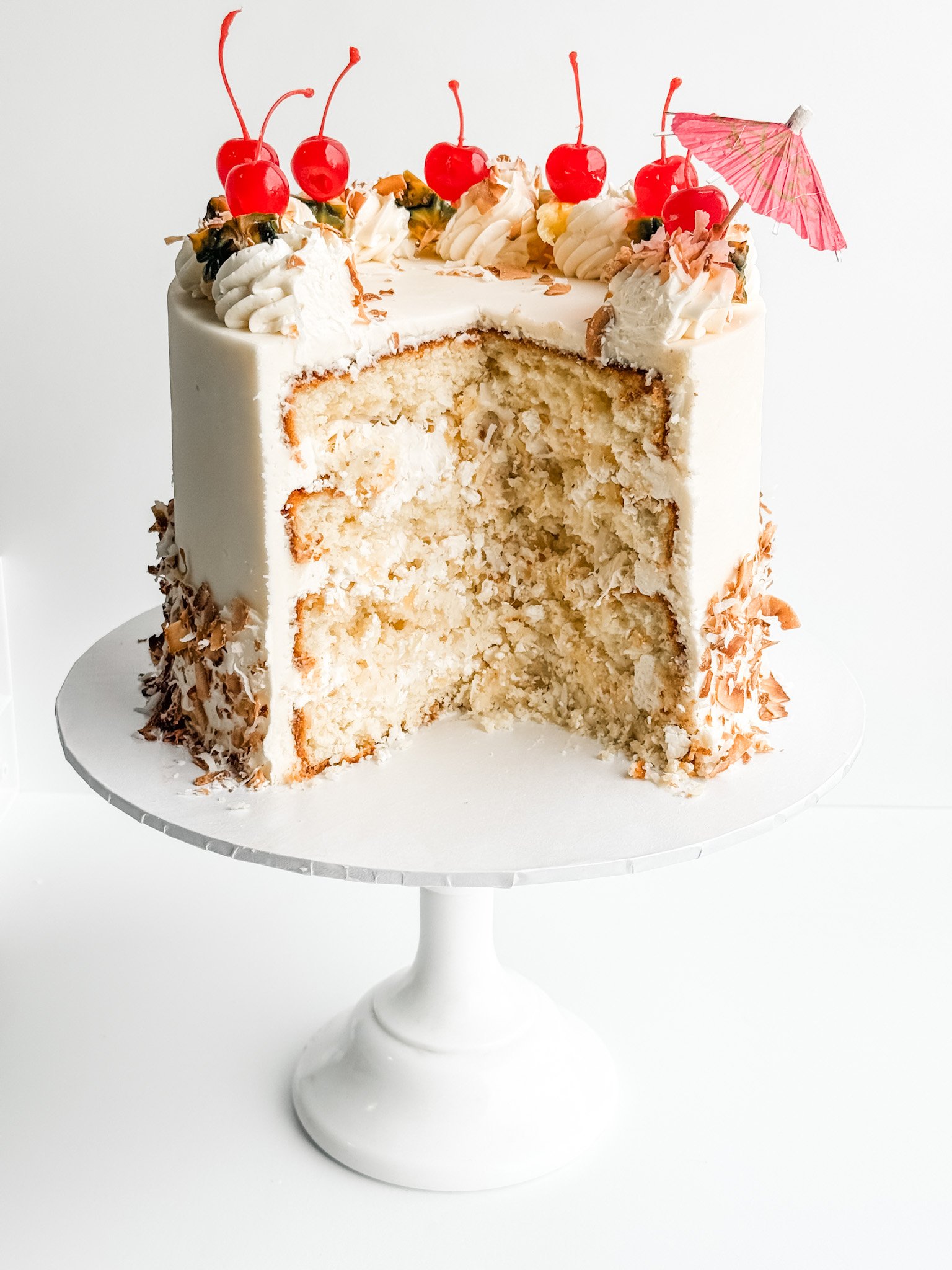 pina colada cake showing the layers and decorated with toasted coconut, pineapple, and cherries