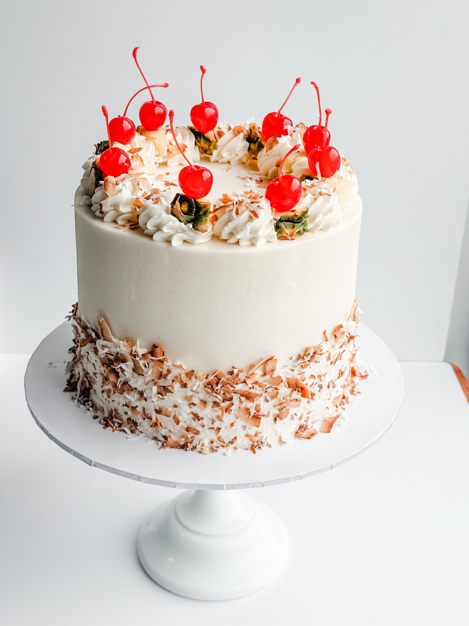 pina colada cake decorated with toasted coconut, pineapple, and cherries