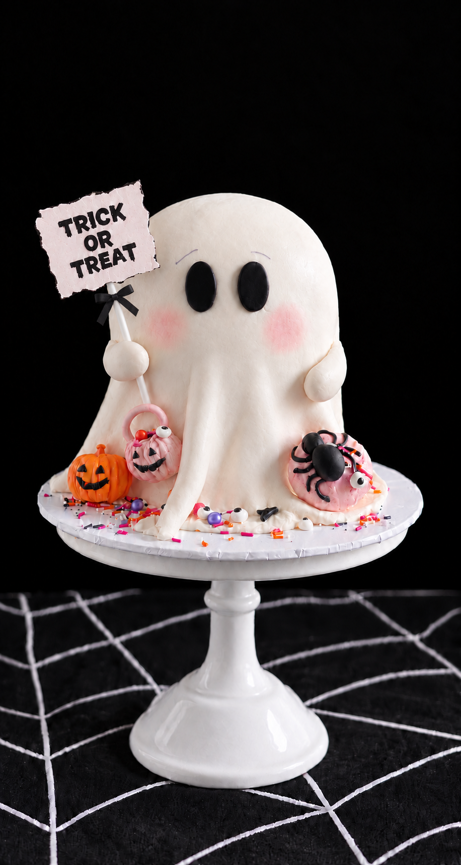 white ghost Halloween cake by Sweet Stacy's Palm Beach with pink cheeks, mini pumpkins, spooky spiders, candy eyeballs and a Trick or Treat sign
