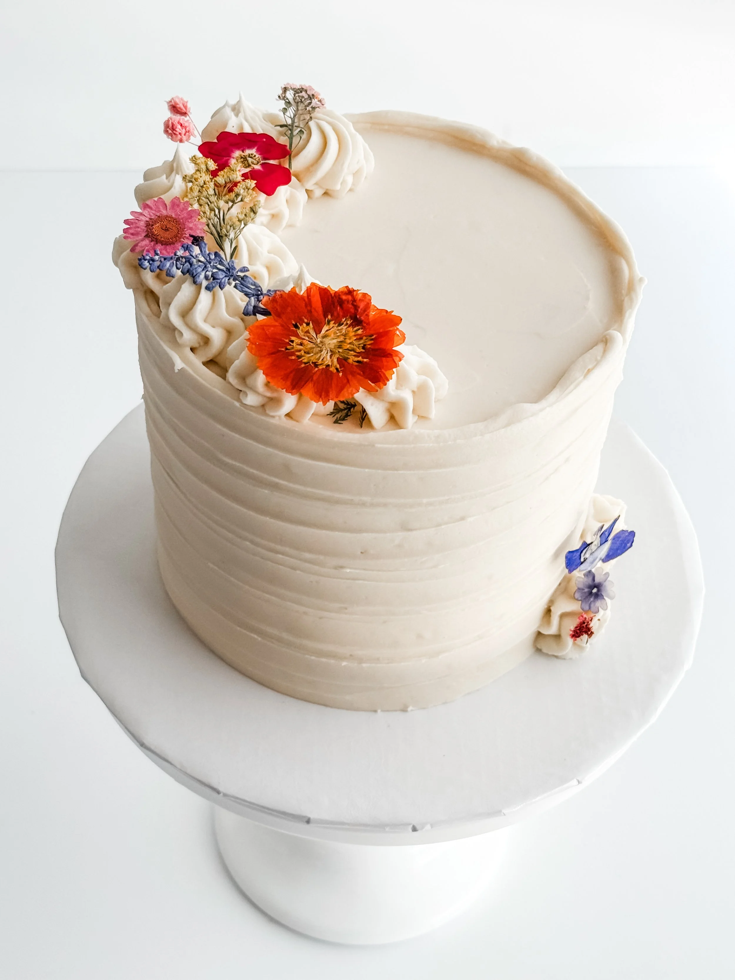 cake on a stand decorated with white frosting and flower buttercream