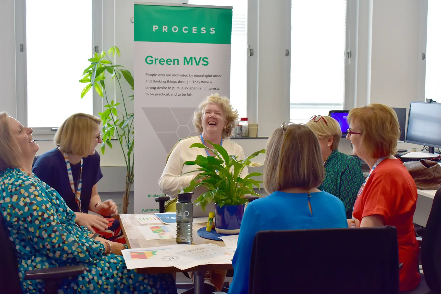 three women in a meeting laughing together with a pull up banner behind them