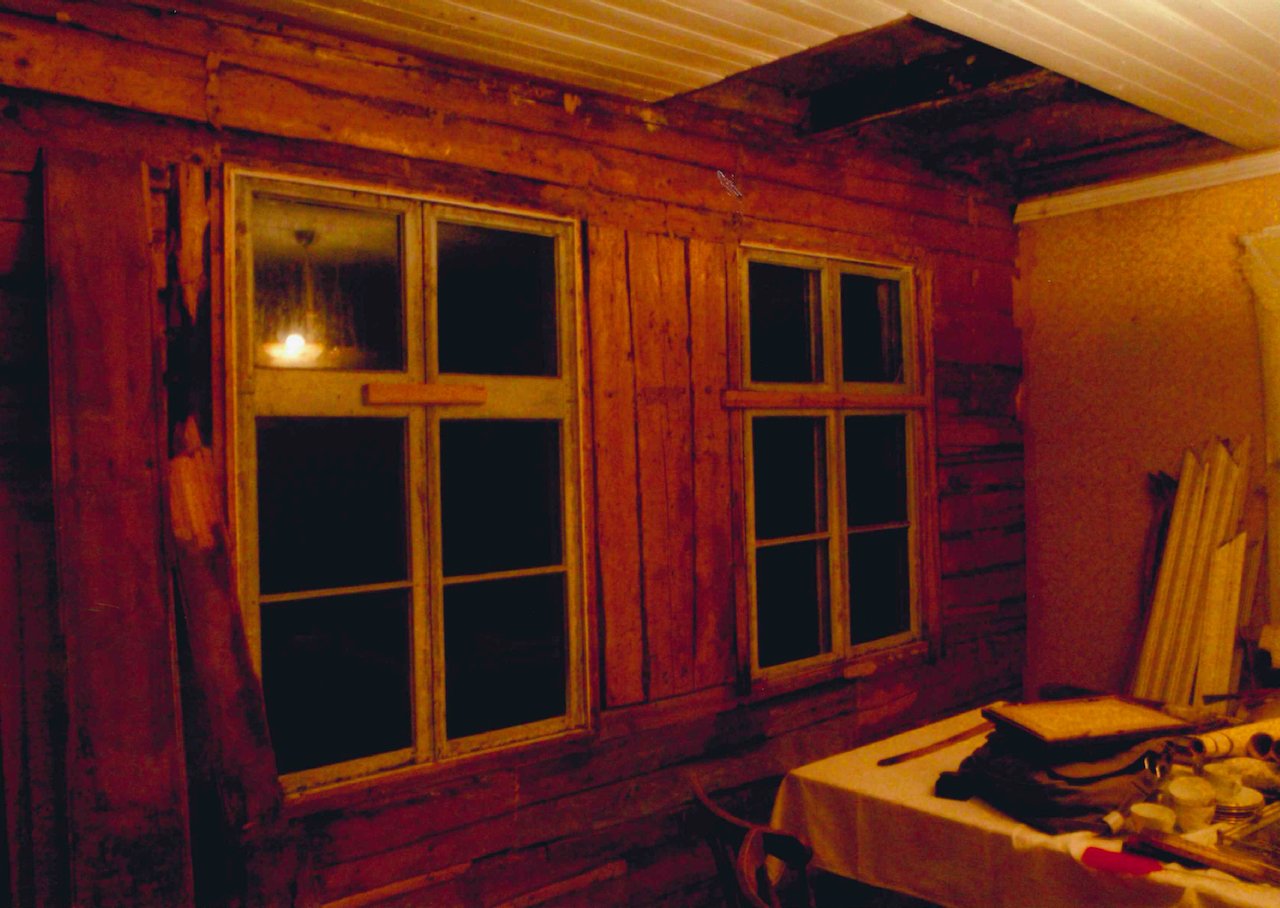 Interior of a room under construction with two wooden-framed windows, wooden walls, and various tools and materials on a table.