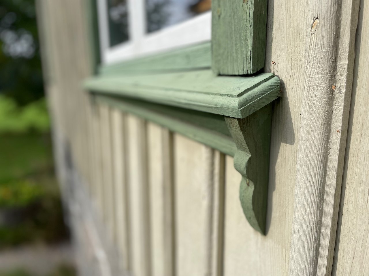Close-up of a wooden exterior wall with a green decorative trim and a window in the background.