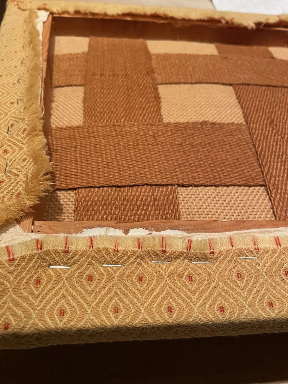 Close-up of a woven fabric pattern inside a partially disassembled picture frame, with nails and staples visible along the edges.