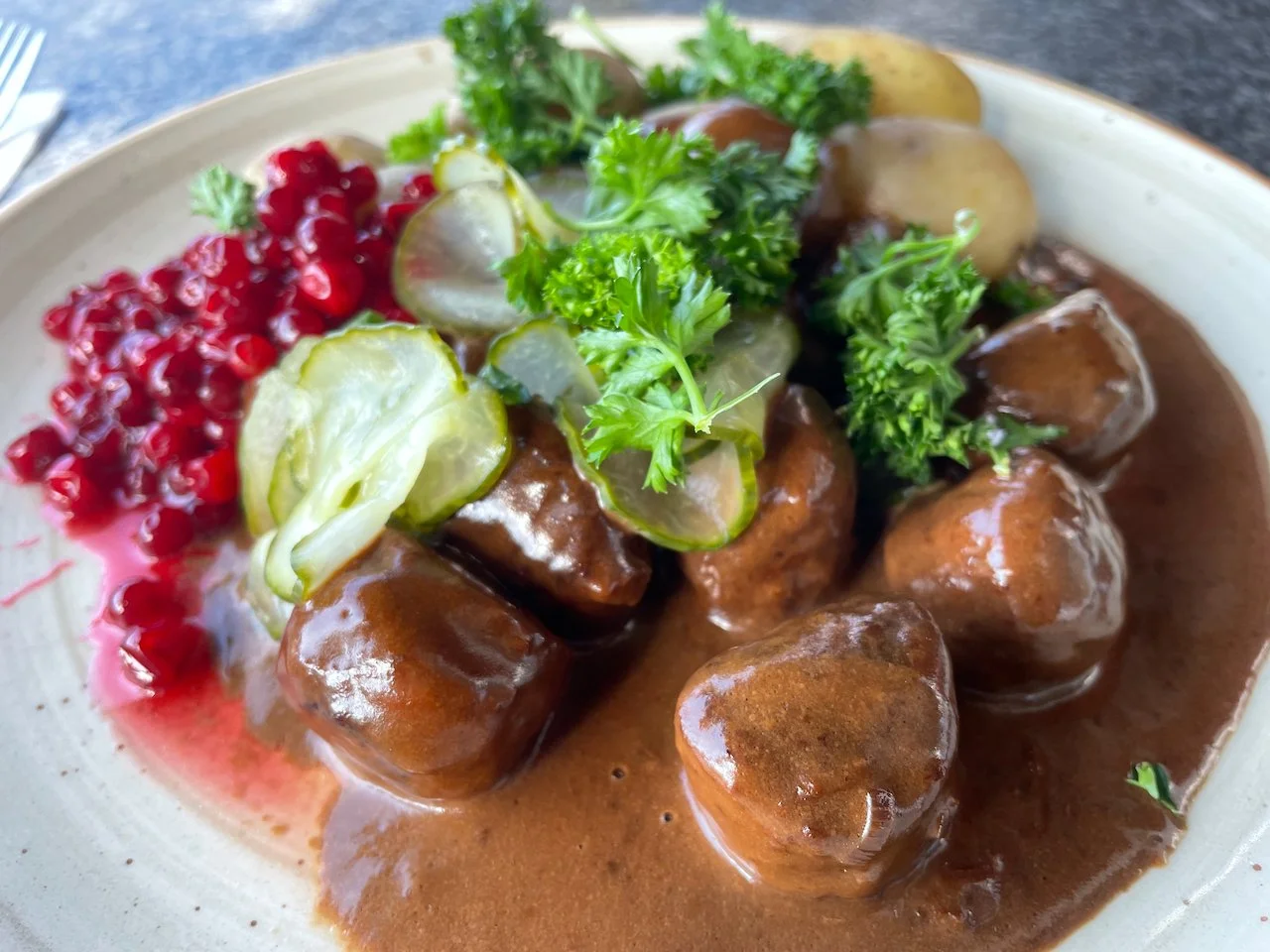 Swedish meatballs with potatoes, pickles, parsley, and lingonberry jam  served on a white plate.