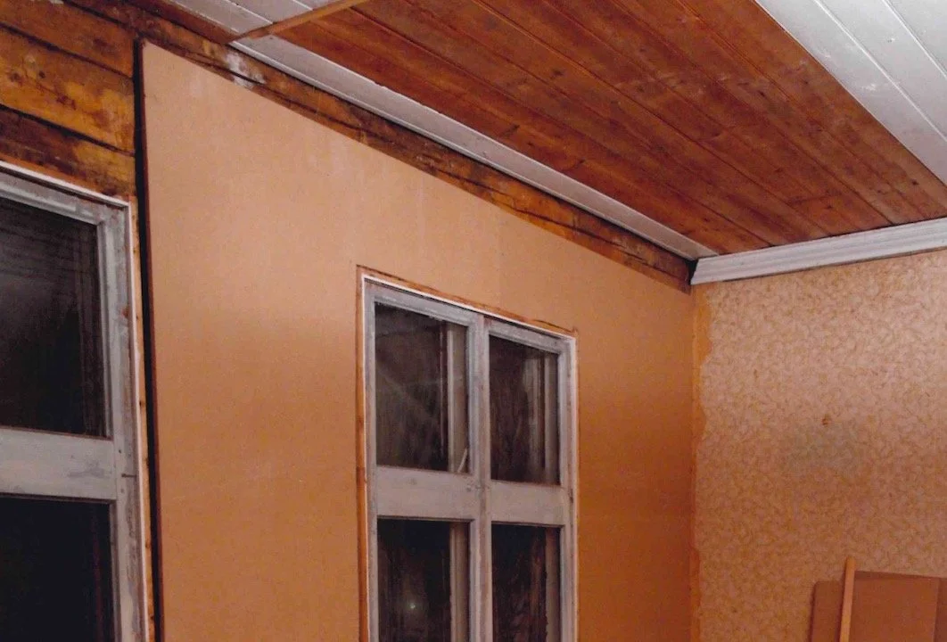 Close-up of an interior room with wooden ceiling, orange walls, and two windows with white frames.