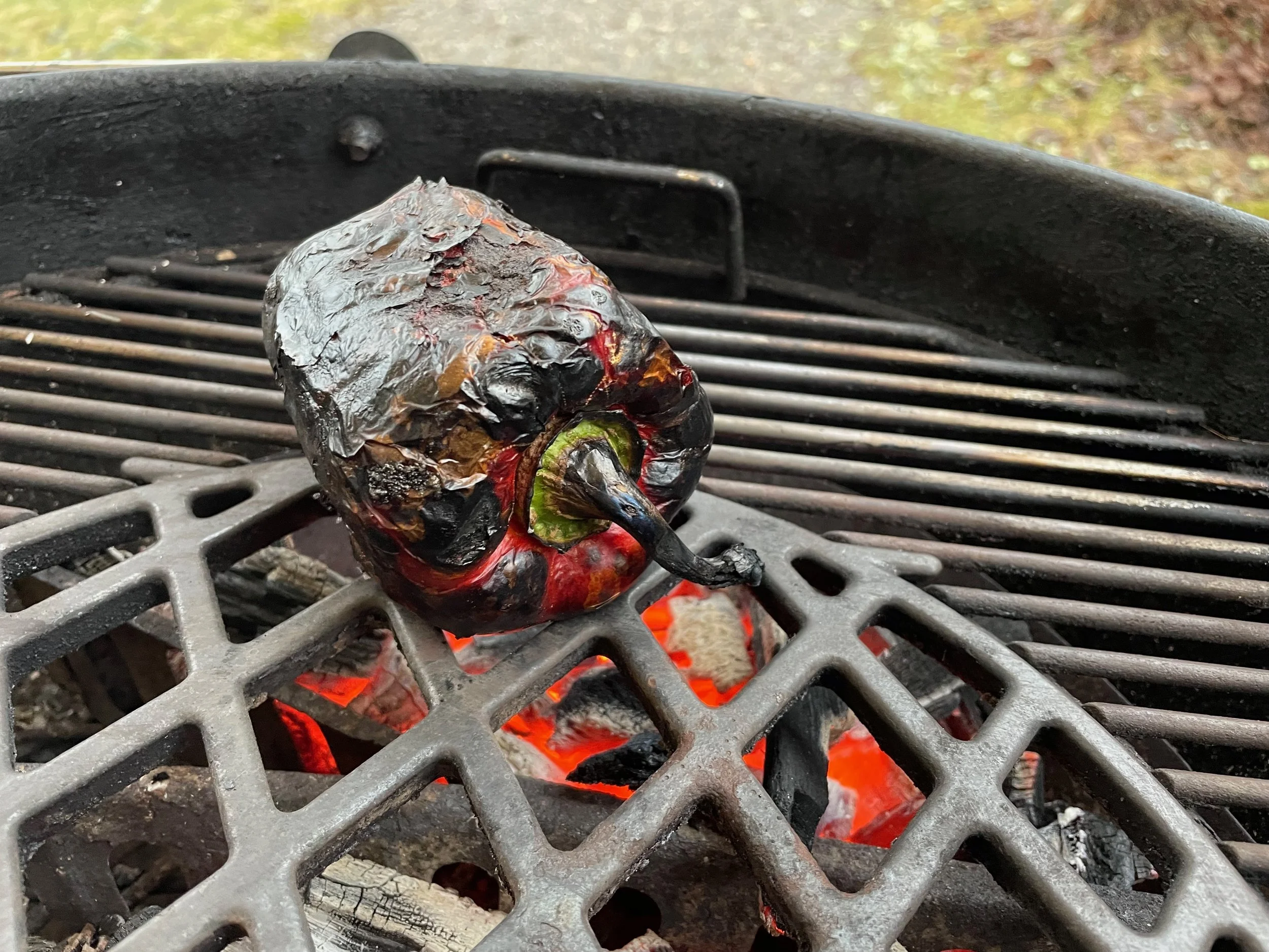 A charred bell pepper on a grill over red-hot charcoal.