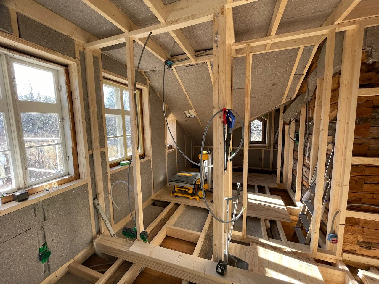 Interior view of a home under construction, showing wooden framing, electrical wiring, and windows.