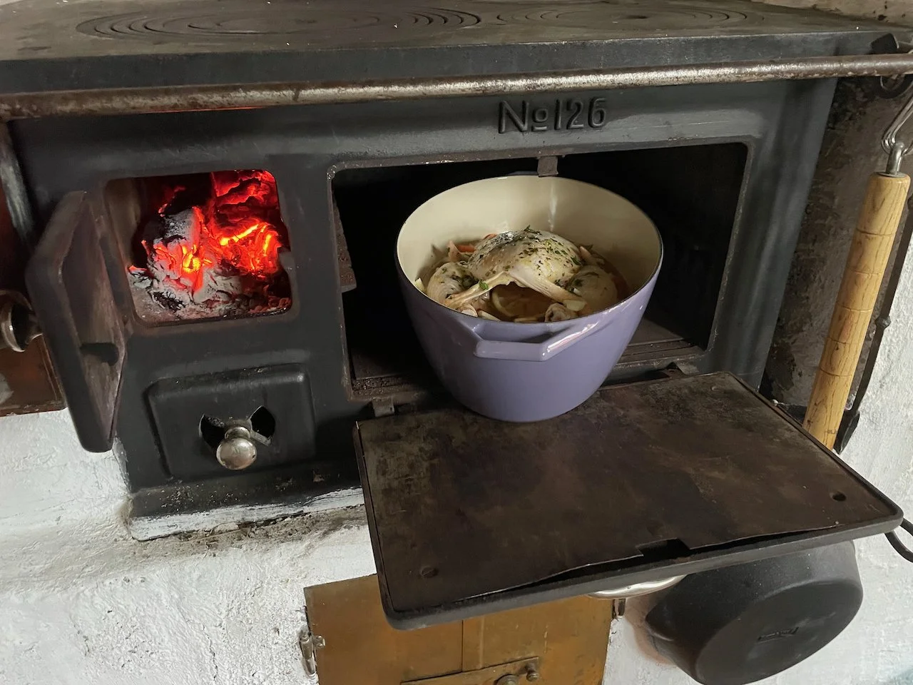 Cooking chicken in a white bowl inside a vintage wood stove with red glowing coals on the left side.