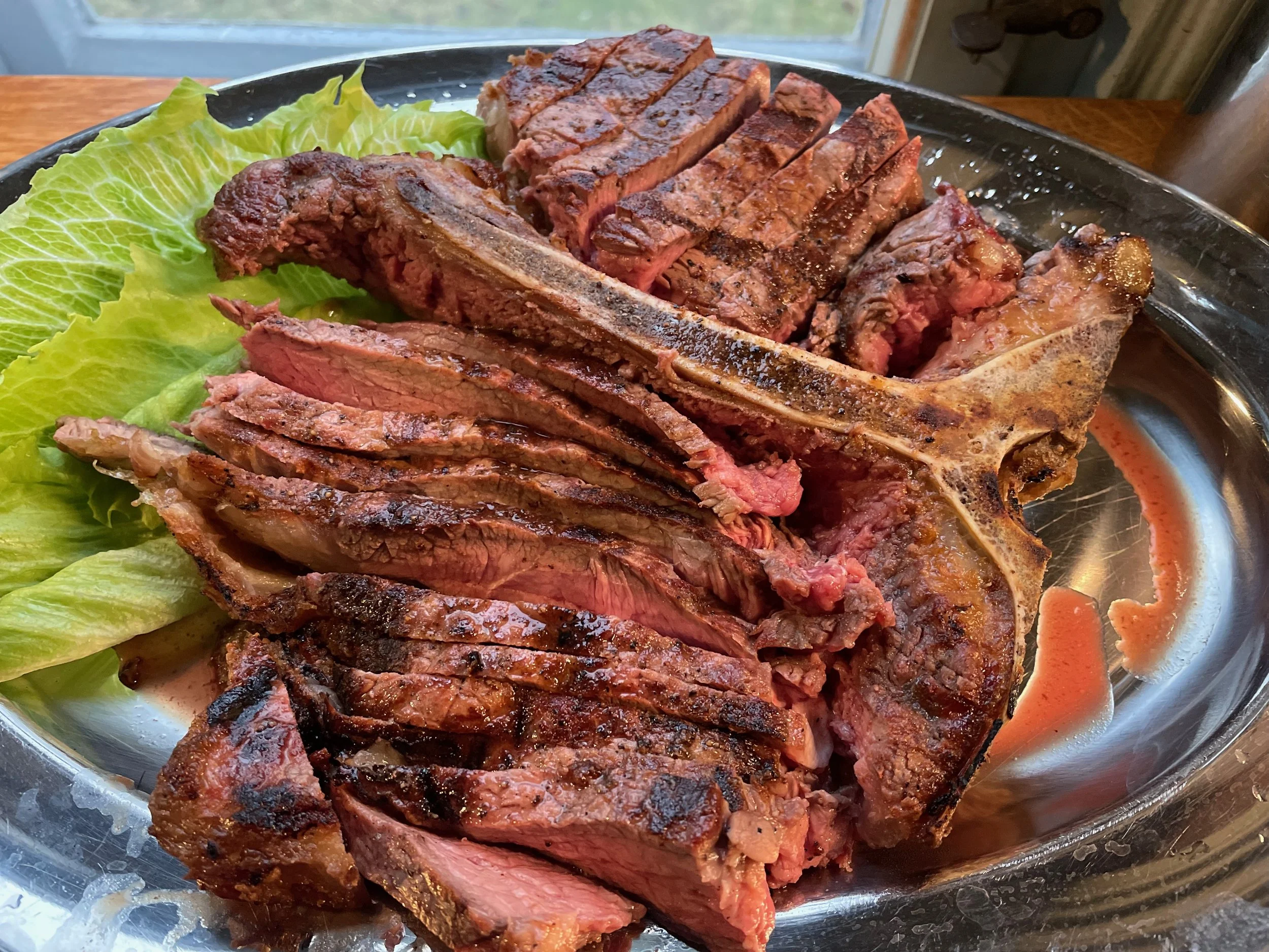 Sliced prime rib with a bone and green lettuce on a metal platter.