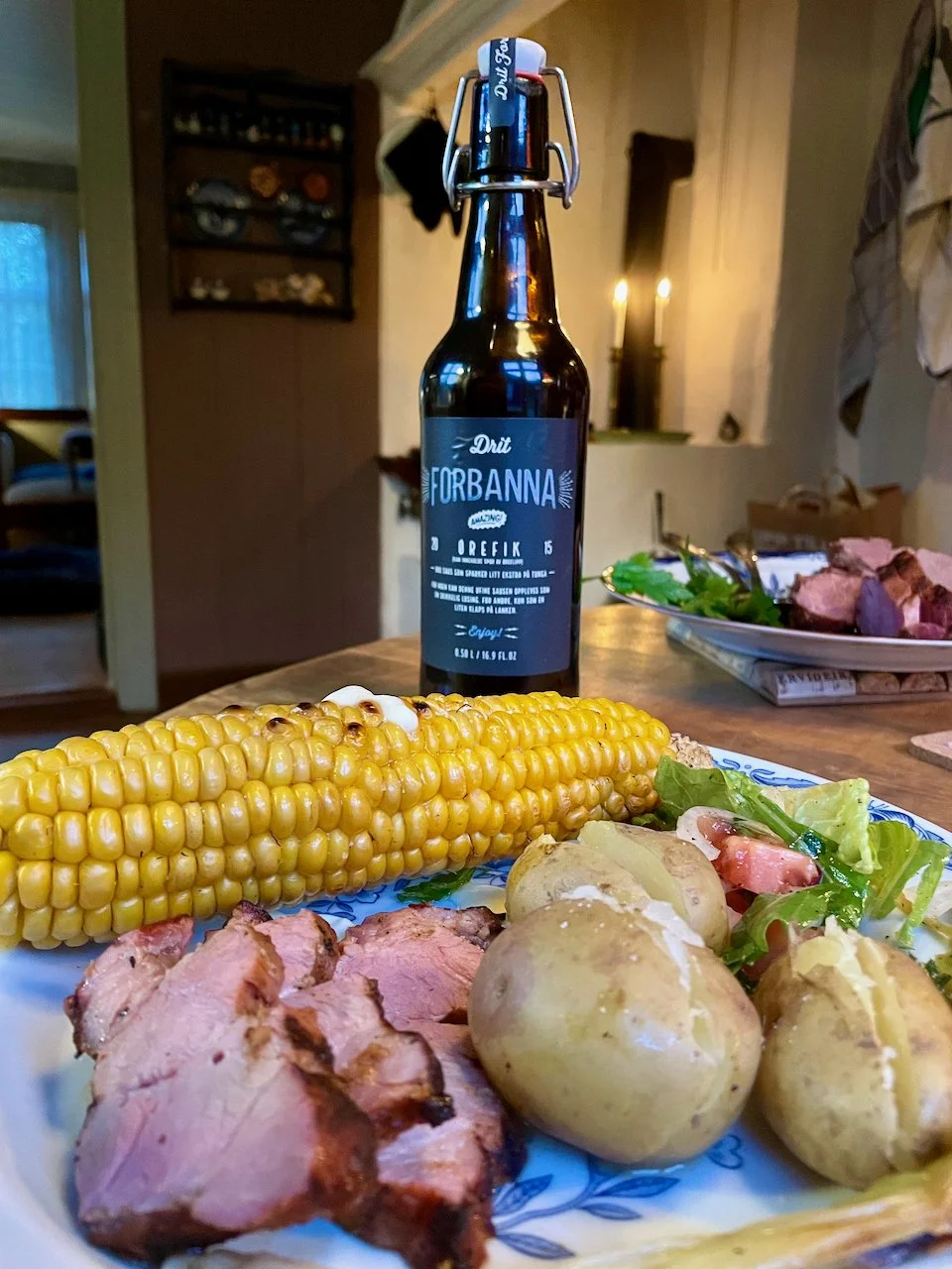 Dish with meat, sweet corn, potatoes with a bottle and kitchen in the back
