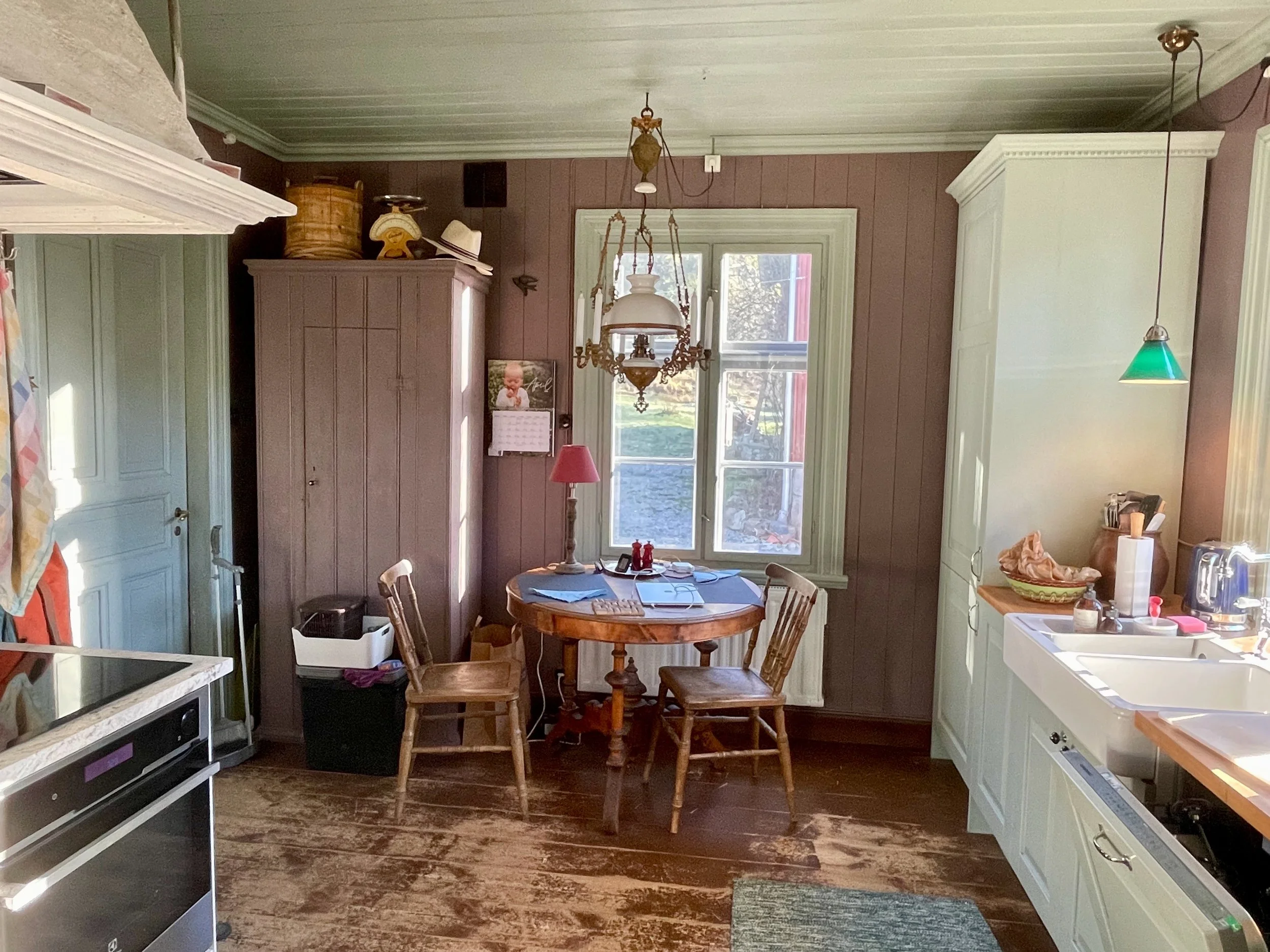 A cozy kitchen with a small dining table and chairs near a large window, with kitchen appliances and cabinets around.