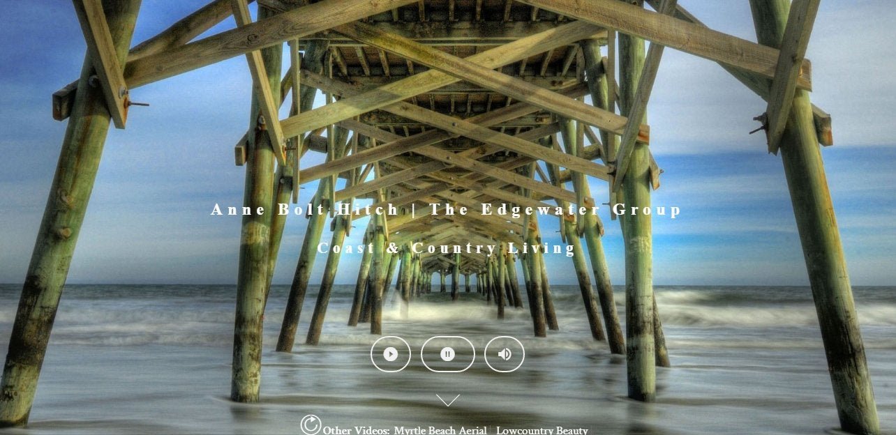 View of a wooden pier from underneath, extending over the ocean with waves, featuring sky and horizon in the background. Text overlay reads: Anne Bolt Hirch, The Edgewater Group, Coast & Country Living.