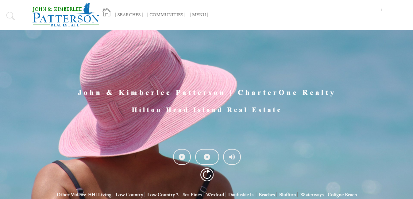 Real estate website header with a person wearing a pink sun hat in front of a blue ocean backdrop. Text reads 'John & Kimberlee Patterson, CharterOne Realty, Hilton Head Island Real Estate.' Navigation includes 'Searches,' 'Communities,' and 'Menu.'