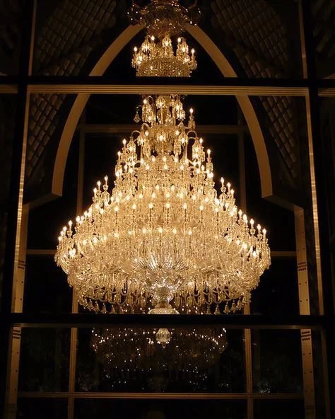 A large, ornate crystal chandelier hanging from a high ceiling in a luxurious setting.