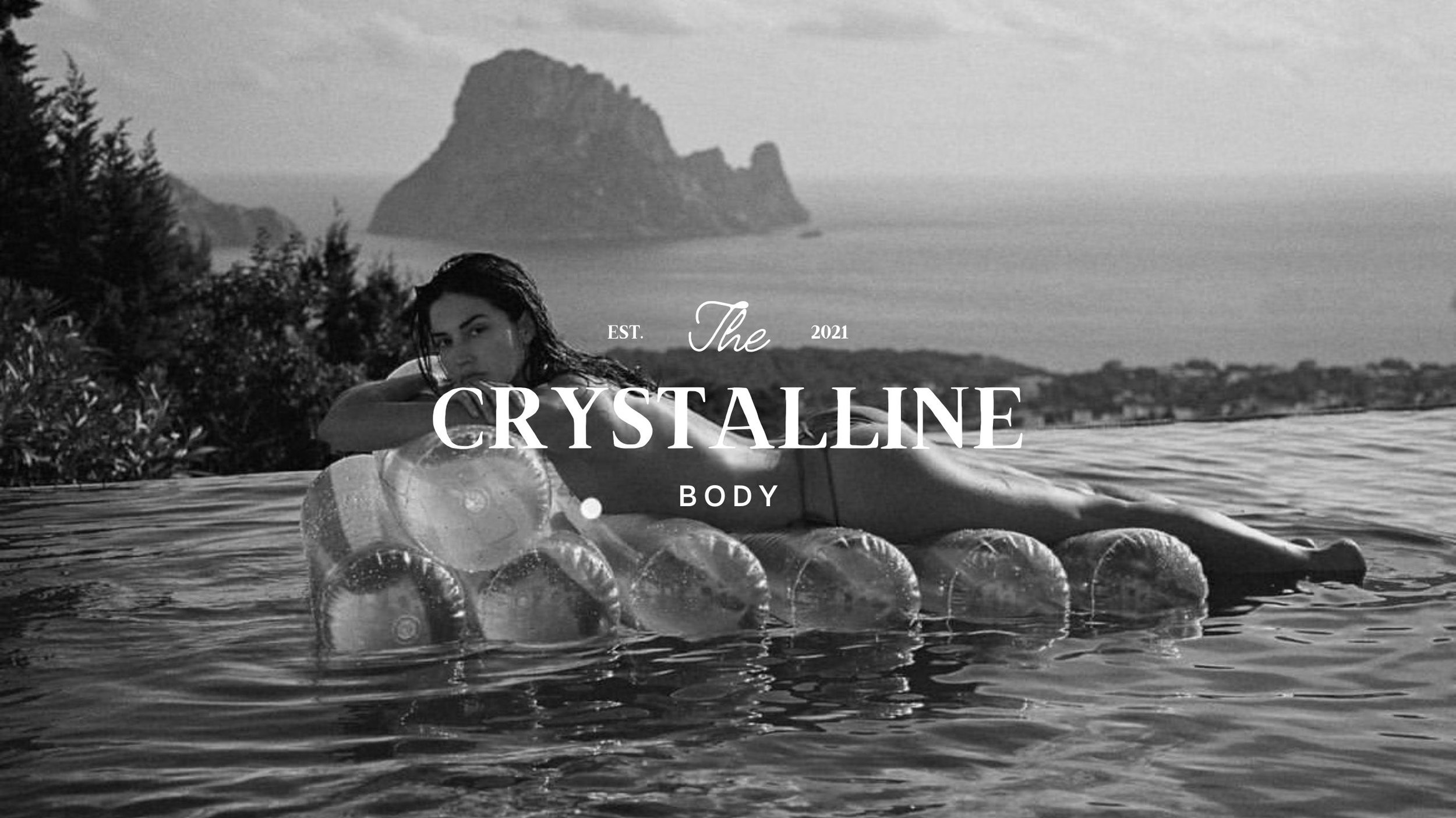 A woman laying on a float made of large inflated plastic bottles, in a swimming pool with a scenic mountain and ocean view in the background, in black and white.