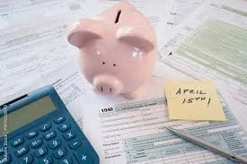 Pink piggy bank placed on scattered papers with a blue calculator and a yellow sticky note that reads 'April 15th'.