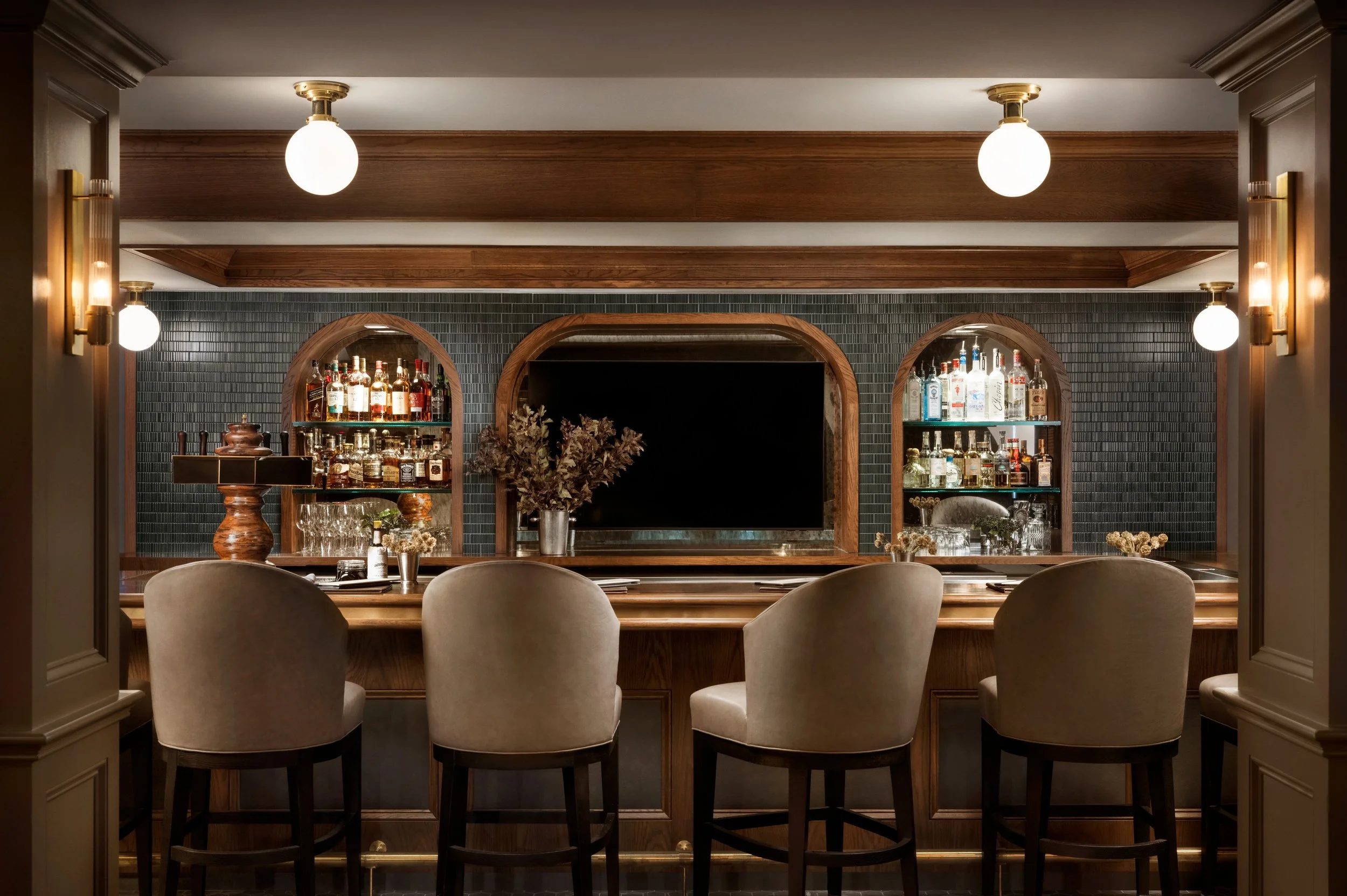 Bar with stools in front of it. Tiled background with shelves of liquor.